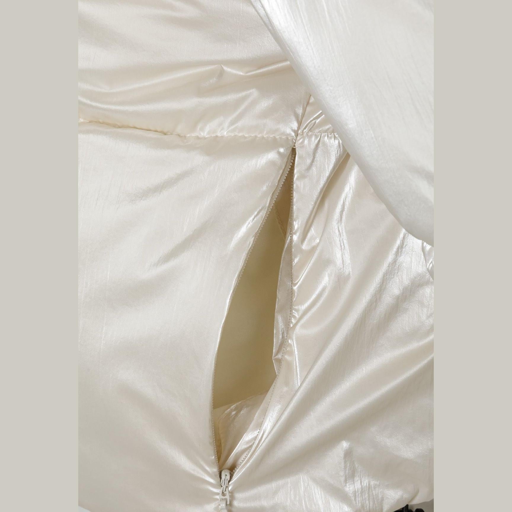 Close-up detail of cream metallic fabric showing quilted texture and zip construction on light background