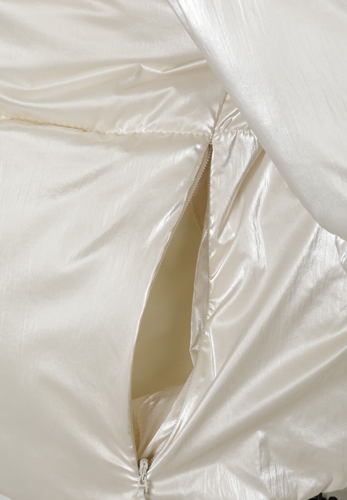 Detail of a cream metallic cropped padded jacket showing zipper and fabric texture.