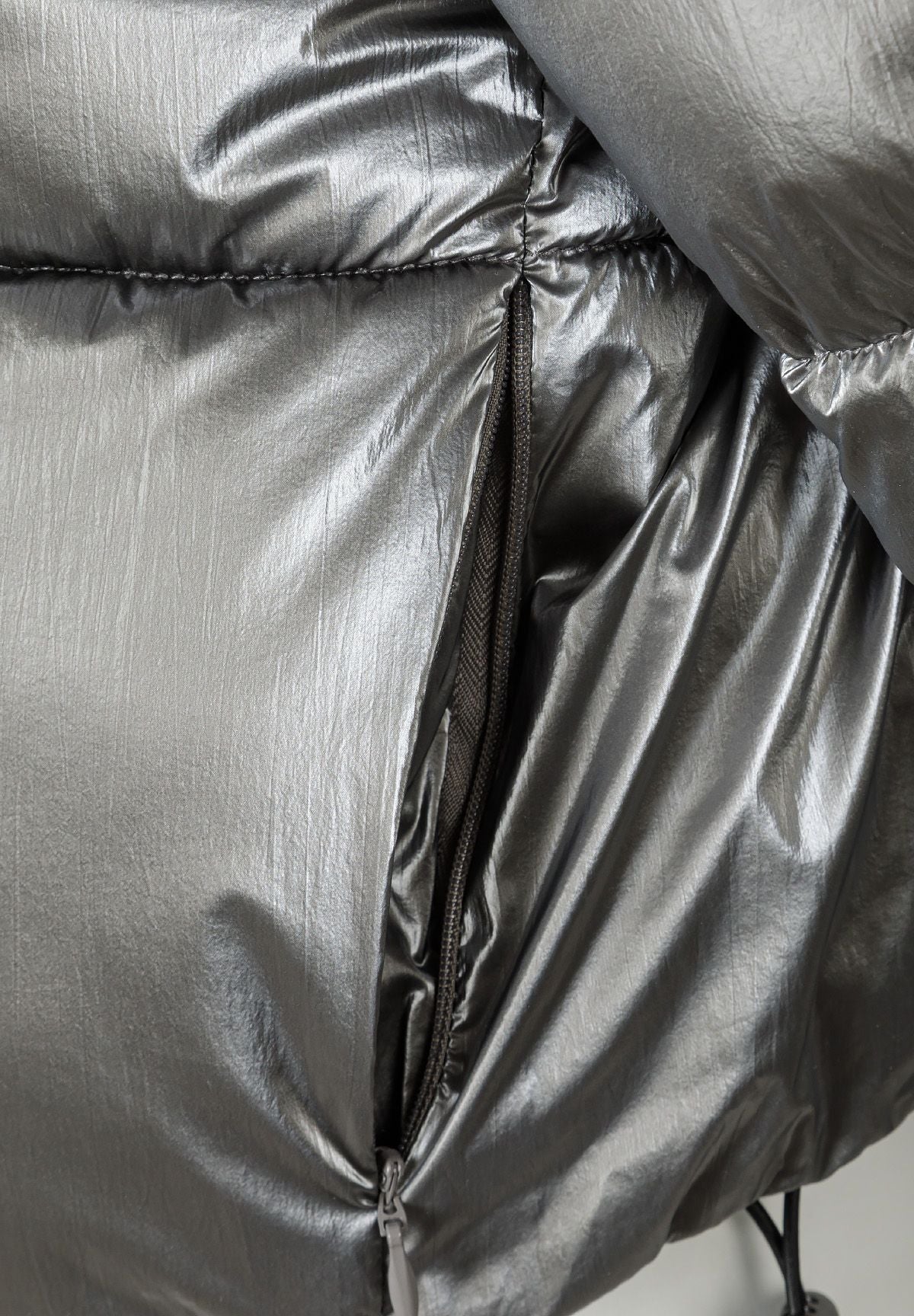 Detail of a women's cropped metallic padded jacket in shiny grey with zip closure.