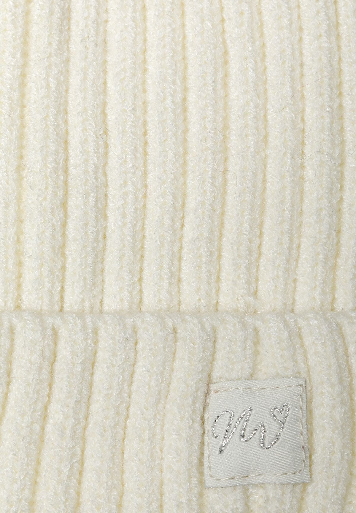 Close-up of a cream knitted rib beanie for babies, featuring a small lurex badge.