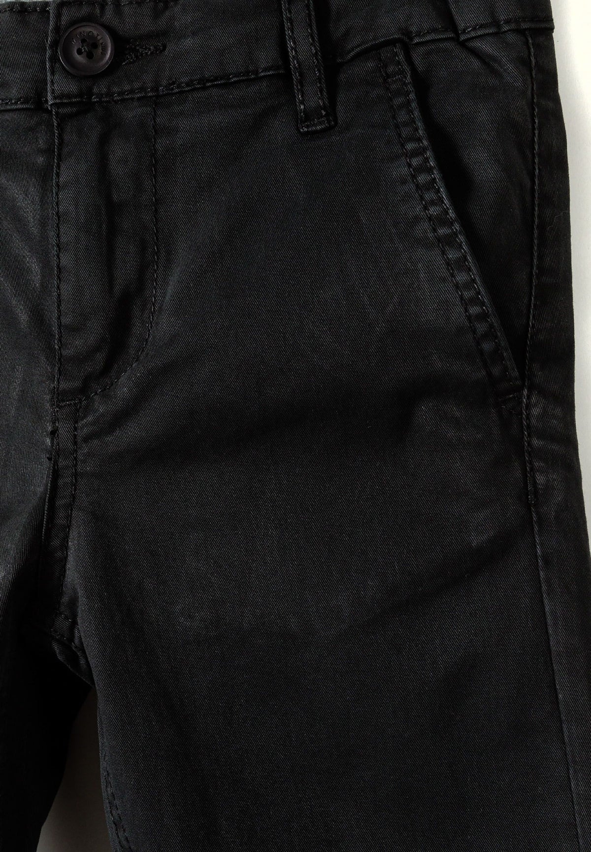 Close-up of black chino waist with dark button, belt loop, fly seam and side pocket.