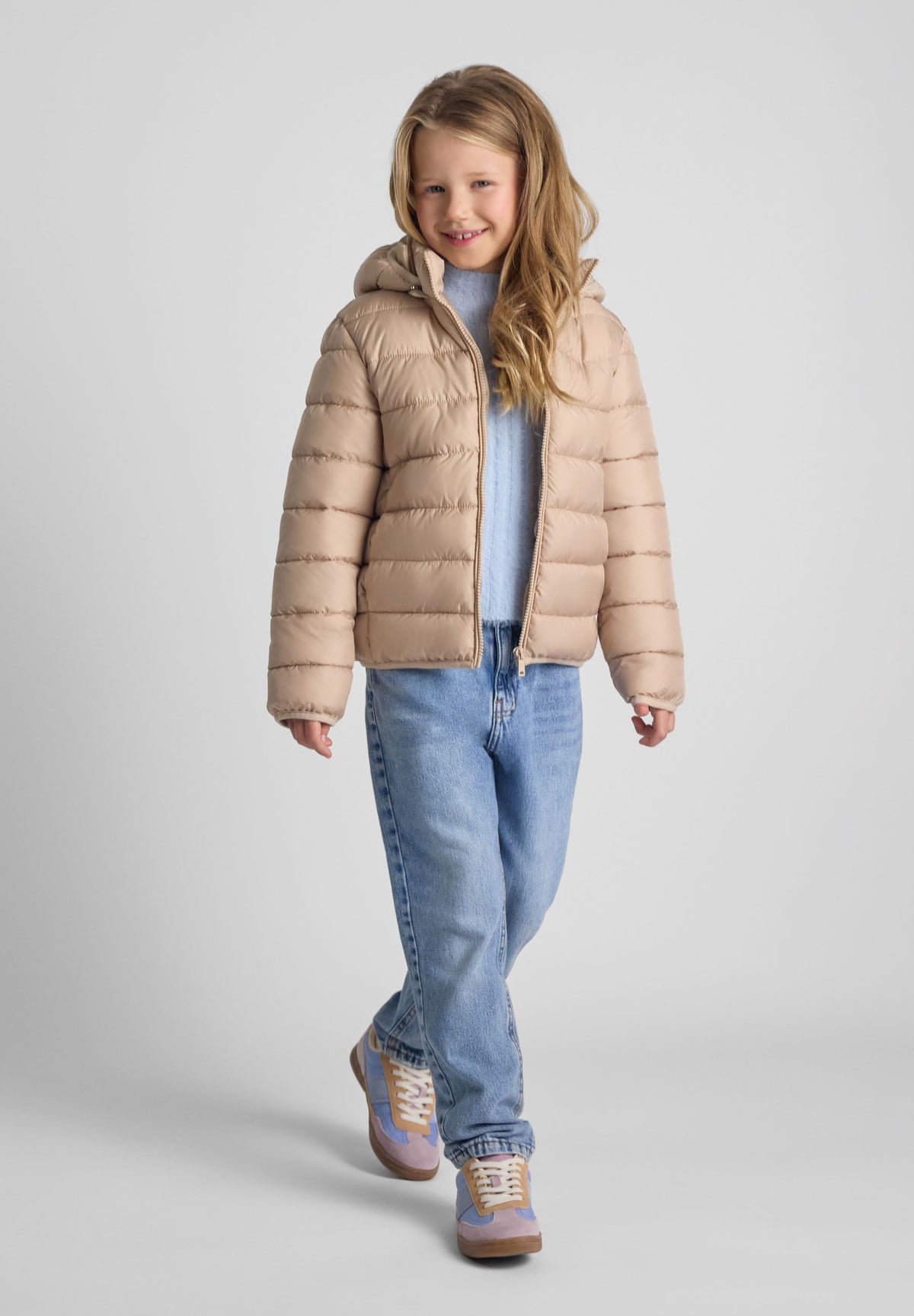 Girl wearing a beige hooded puffer jacket open over a pale blue top.