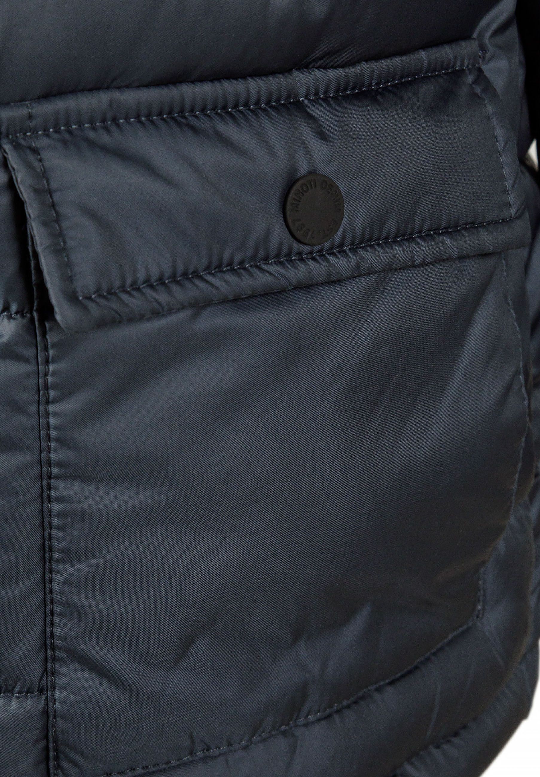 Detail of a navy boys jacket with a rubber badge and flap pocket.