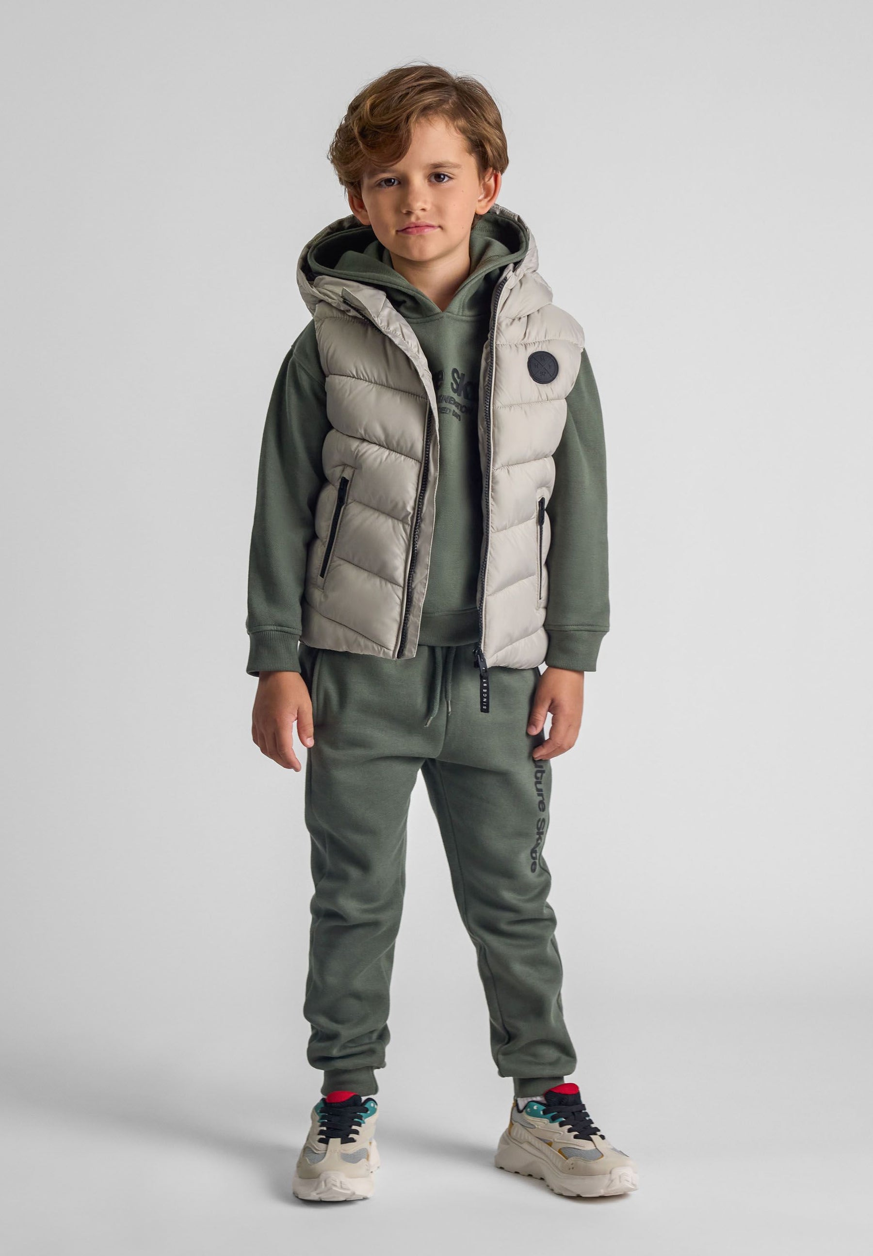Boys grey gilet with fixed hood, full-length zip, and chest badge, front view.