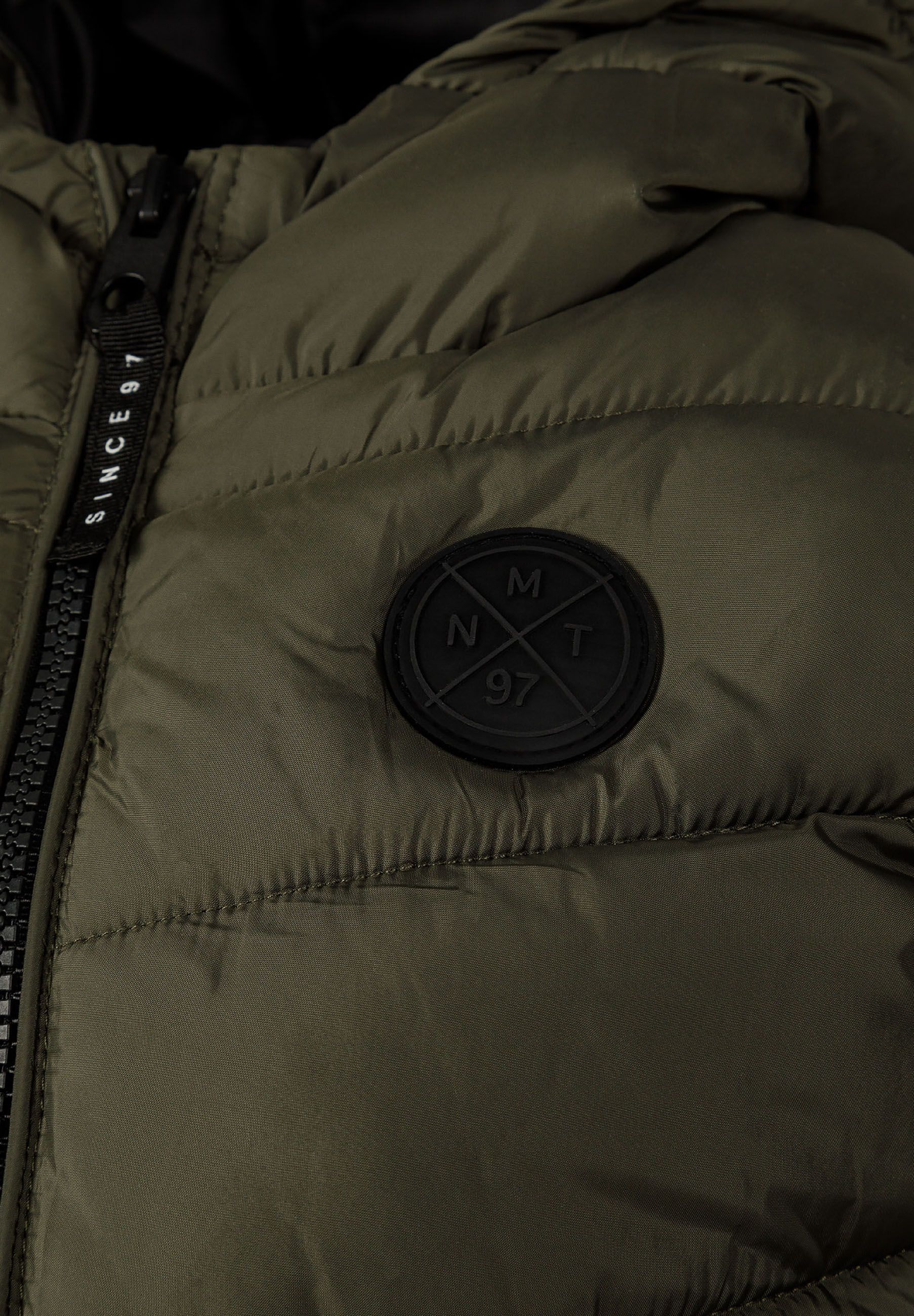 Detail of khaki boys gilet featuring a chest badge and zip closure.