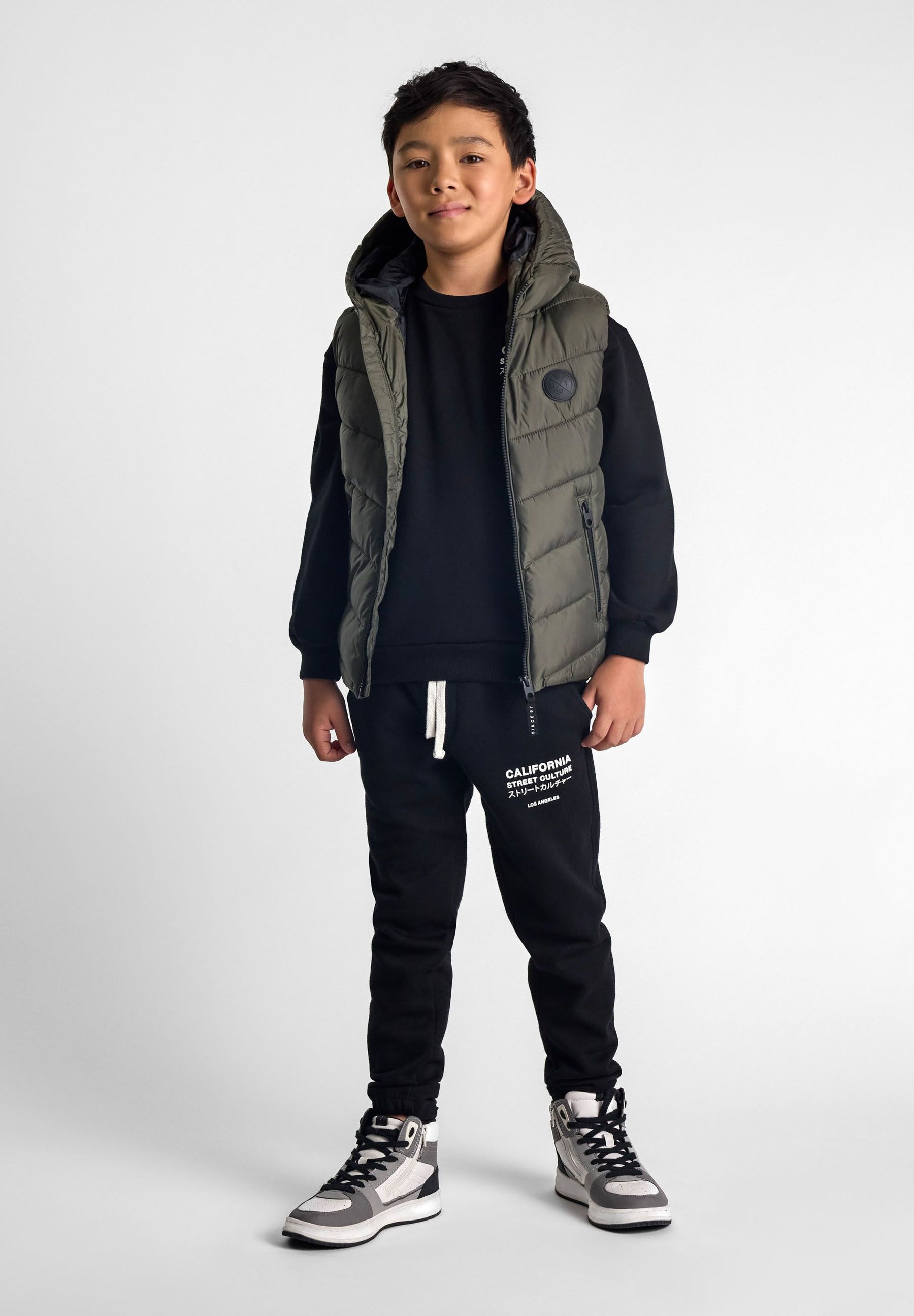 Boys khaki gilet with badge, front view, featuring a fixed hood and zip pockets.