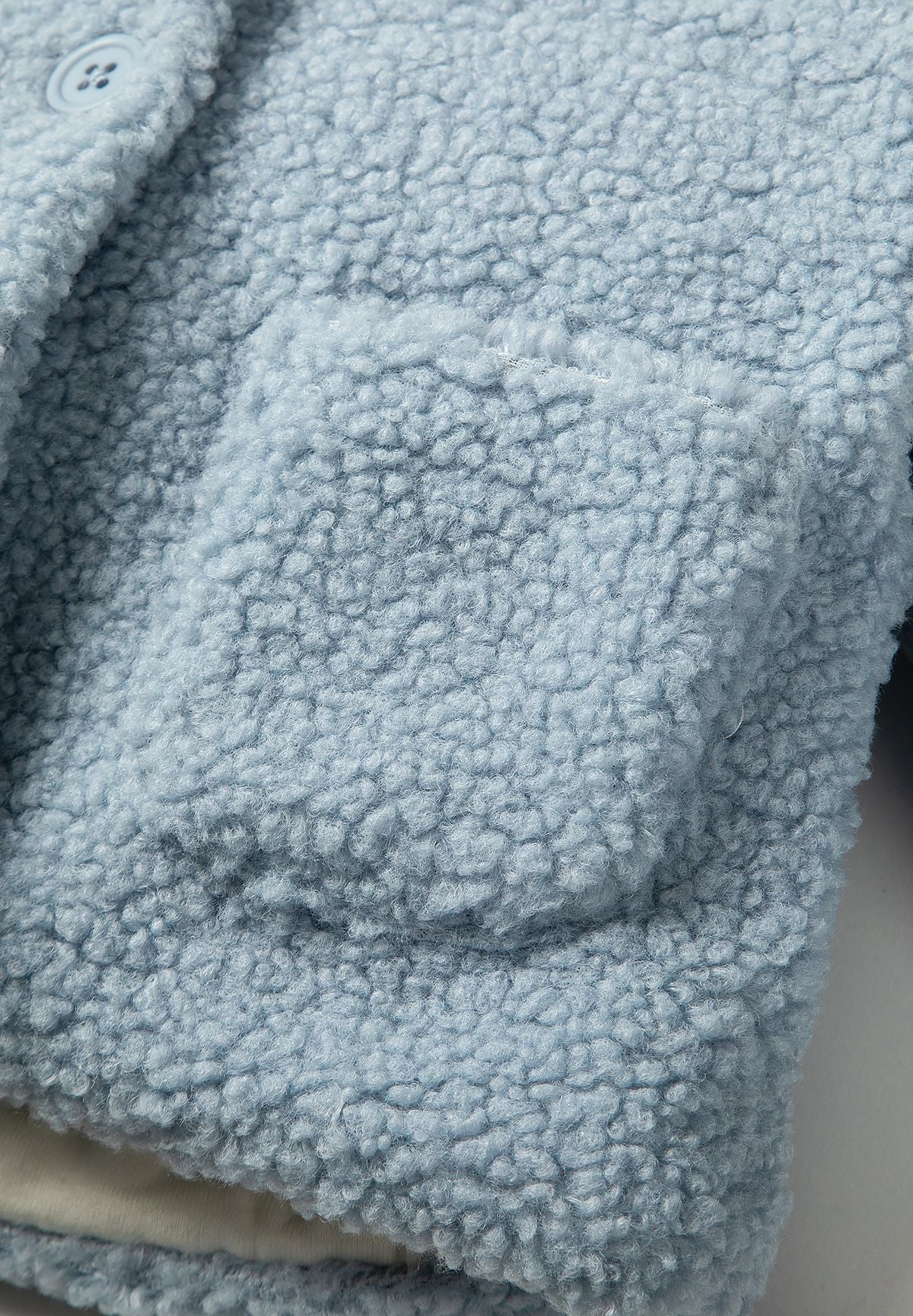 Detail of a light blue teddy baby jacket with button closure and patch pocket.