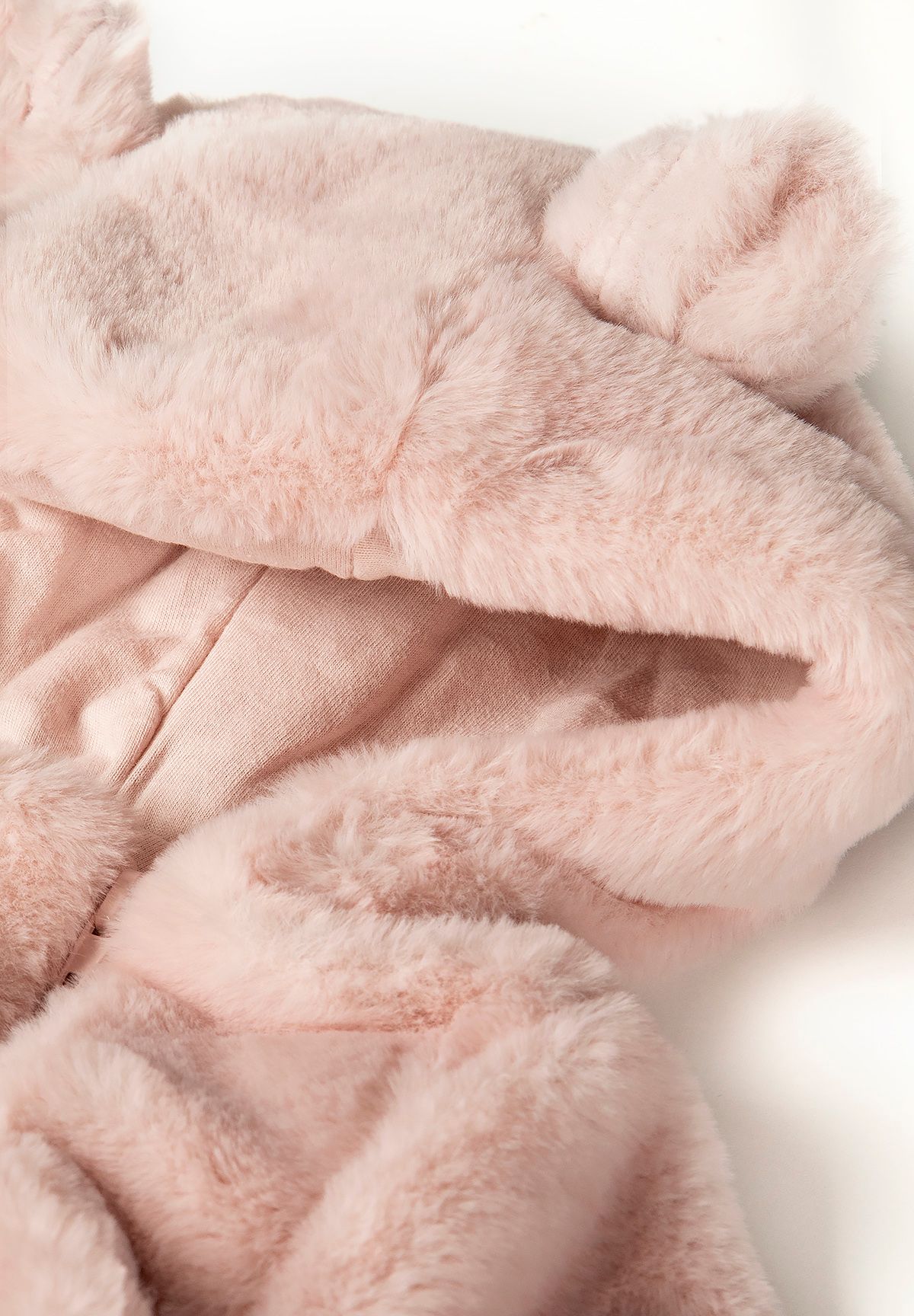 Close-up of light pink faux fur snowsuit hood with 3D ears and soft texture.