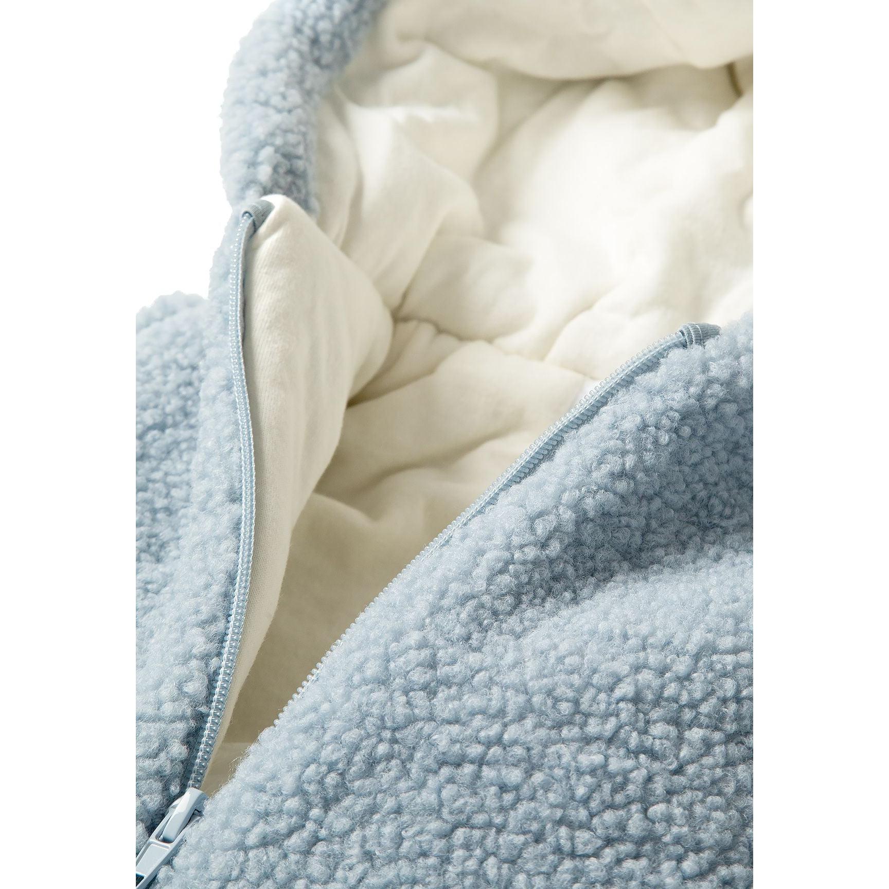 Close-up detail of light blue sherpa fabric texture with full-length zipper and cream jersey cotton lining visible inside