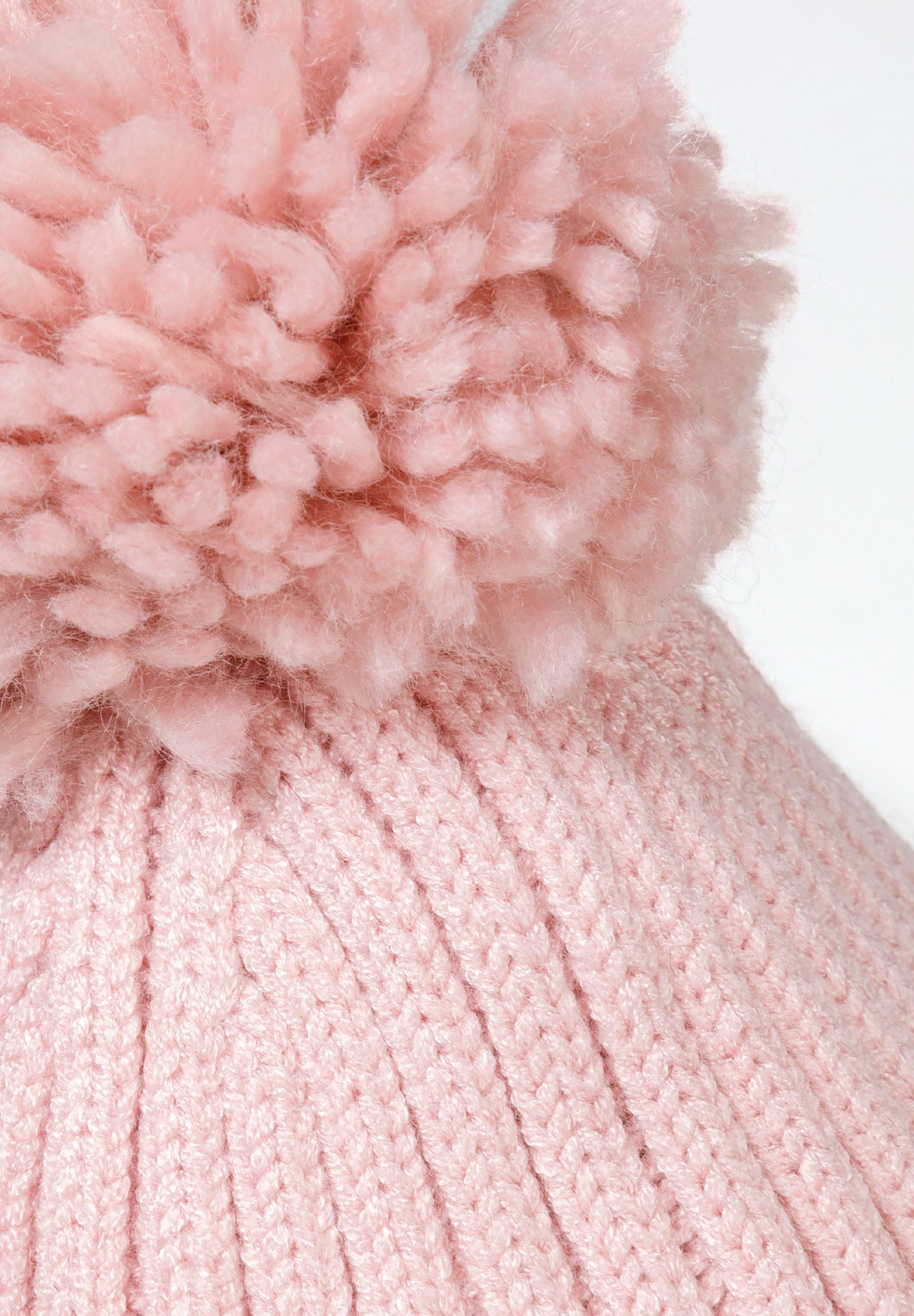 Detail of a ribbed knit hat for girls with a pink pompom on top.