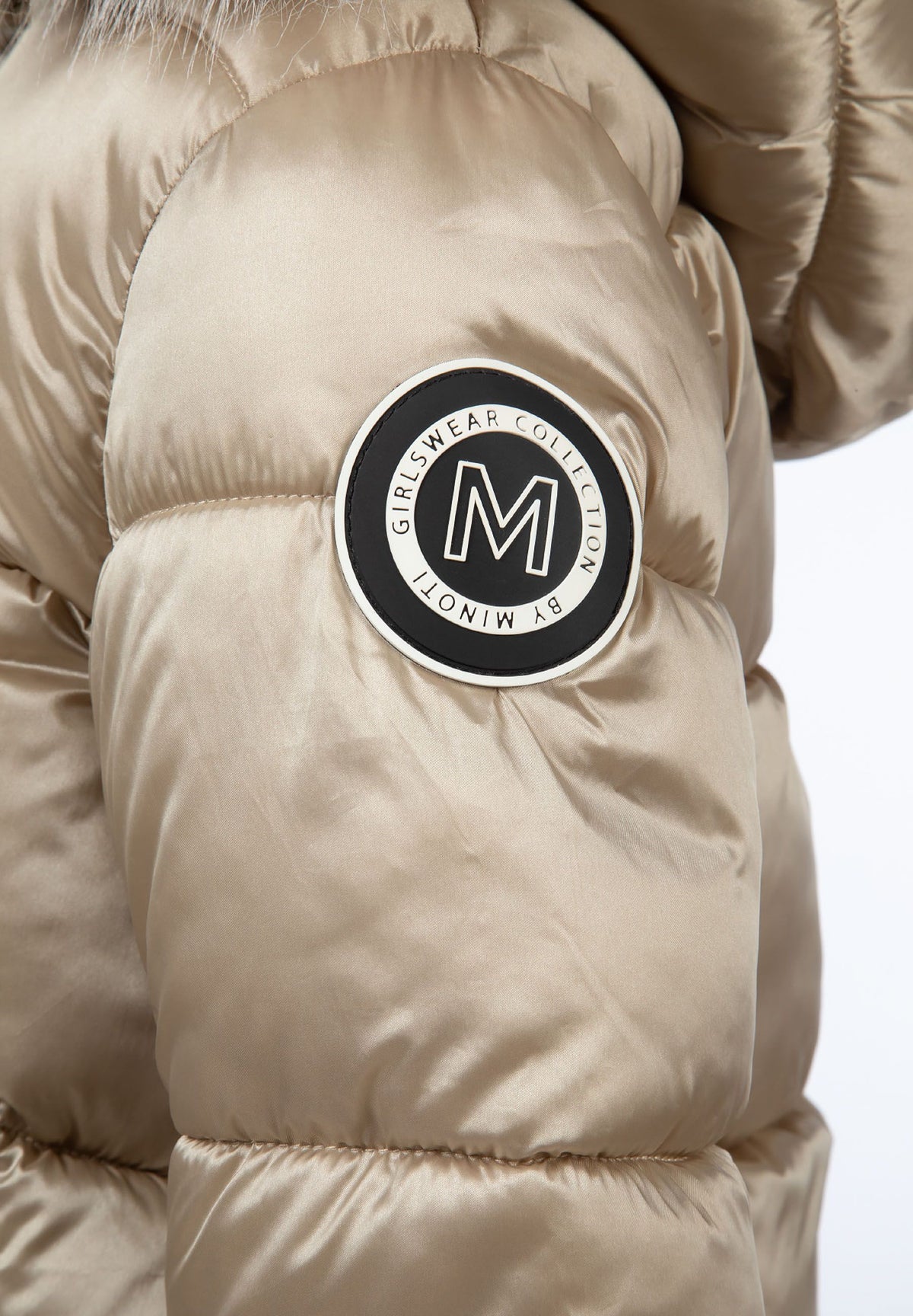 Close-up of the circular black and white Minoti badge on the gold coat sleeve.