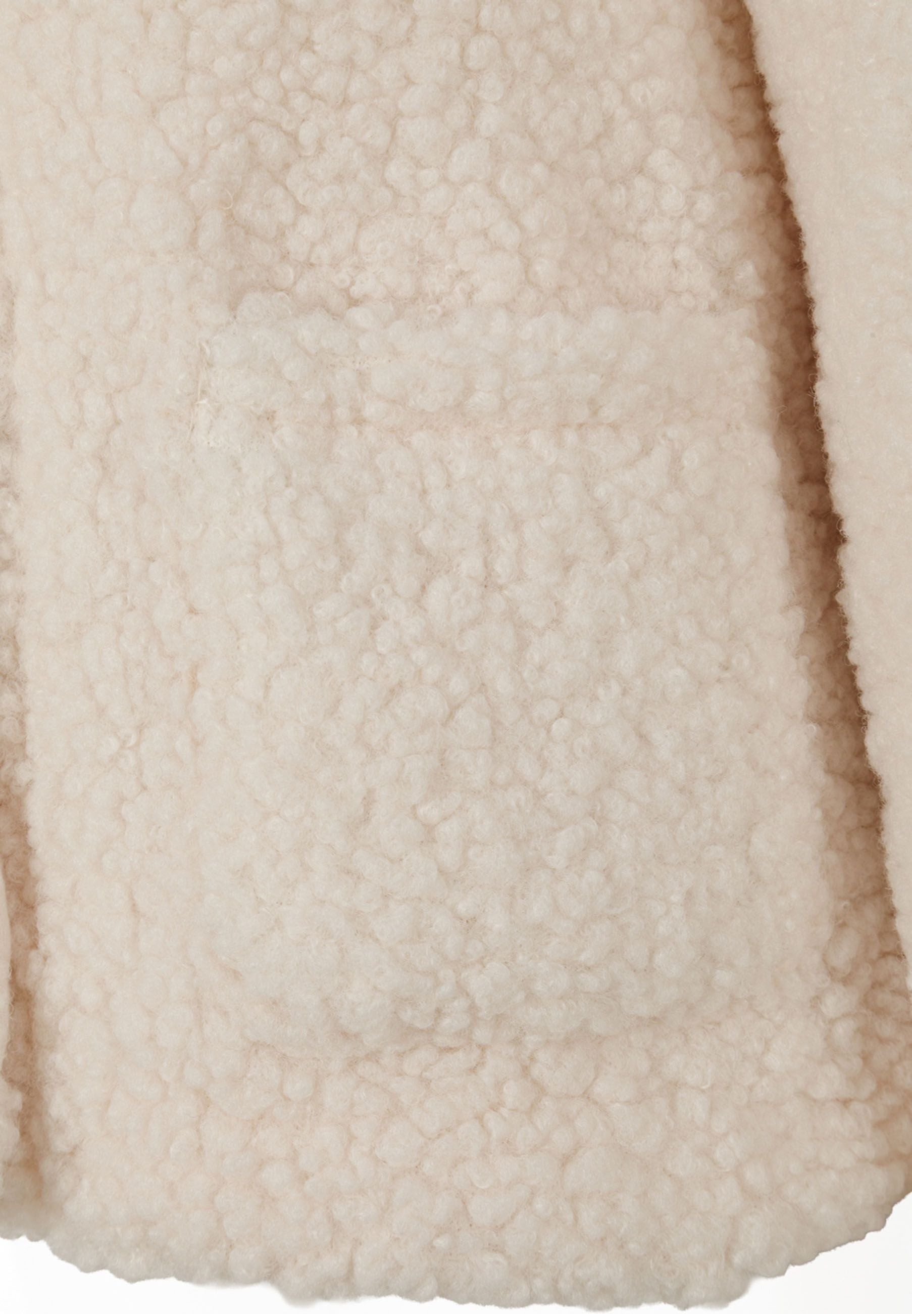 Detail of cream teddy fleece jacket showing soft texture and front patch pocket.