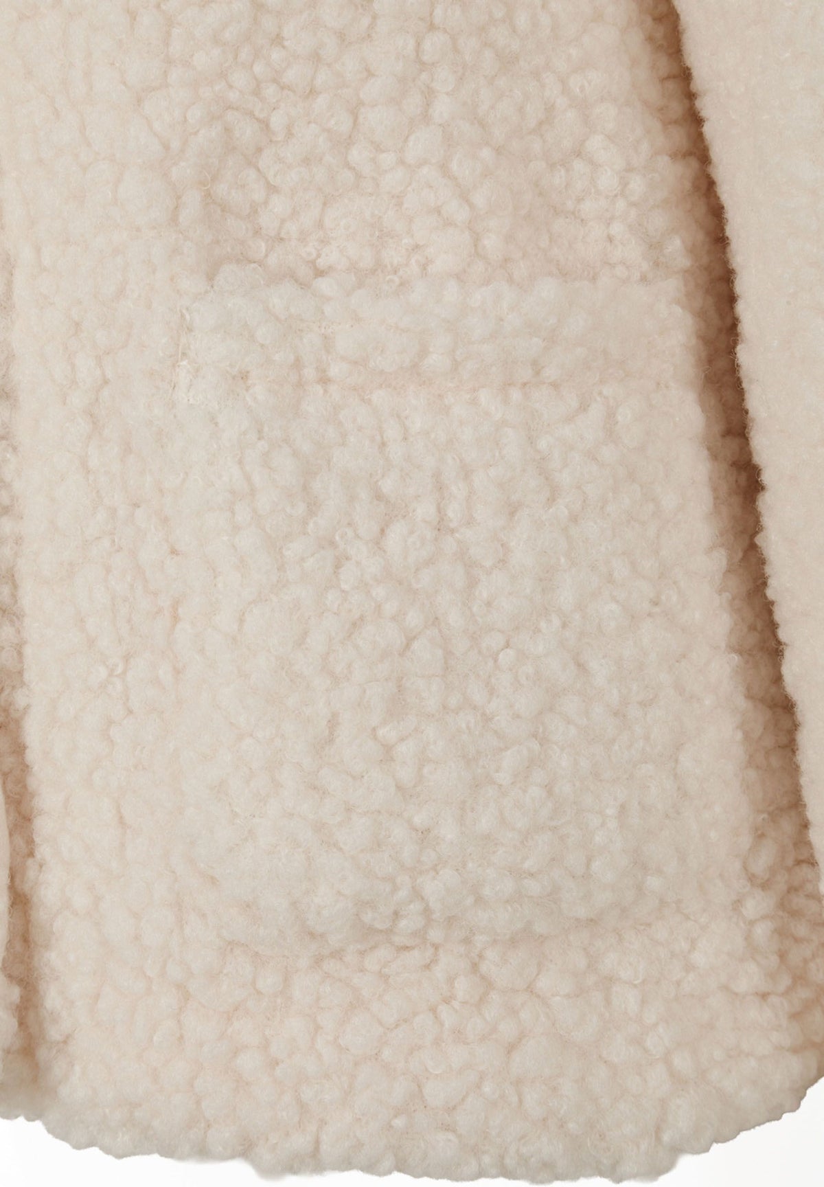 Close-up of a rectangular patch pocket in the cream teddy jacket's curly fabric.