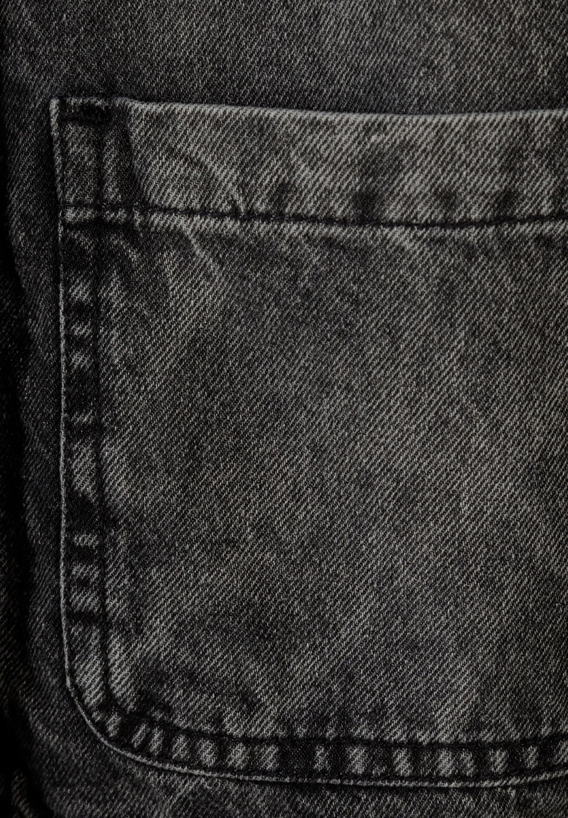 Detail of black acid-wash denim jacket pocket with stitching.