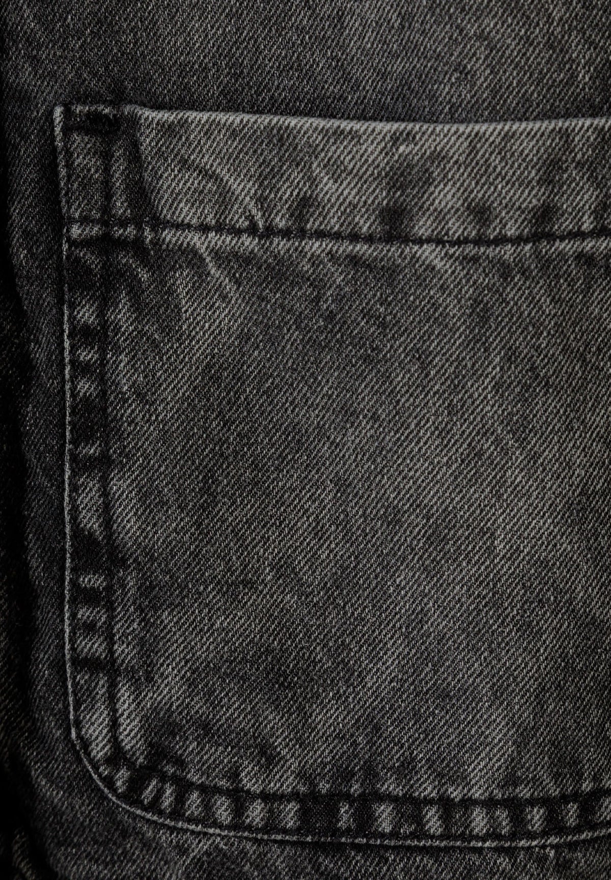 Close-up of a large open-top patch pocket in faded charcoal-black denim.