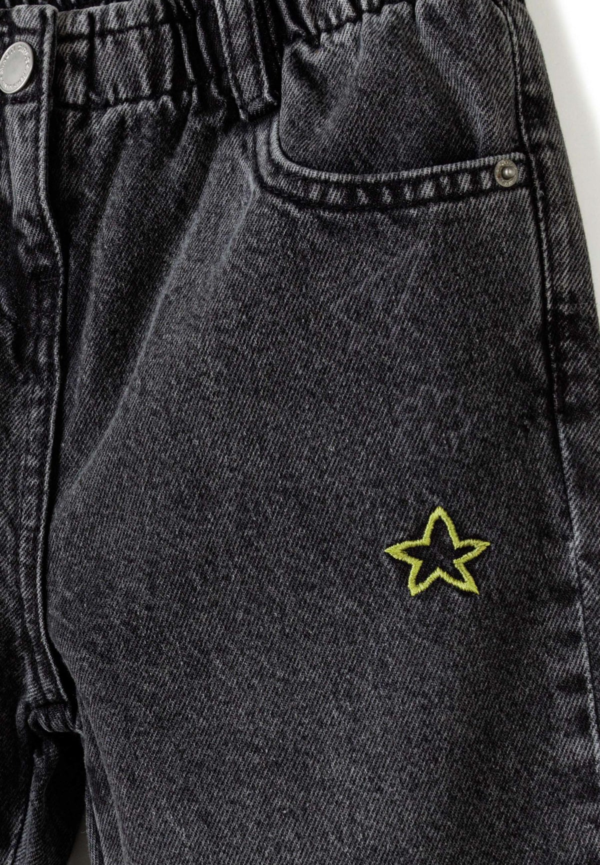 Close-up of washed black jeans showing elastic waist, front pocket and yellow outlined star embroidery.