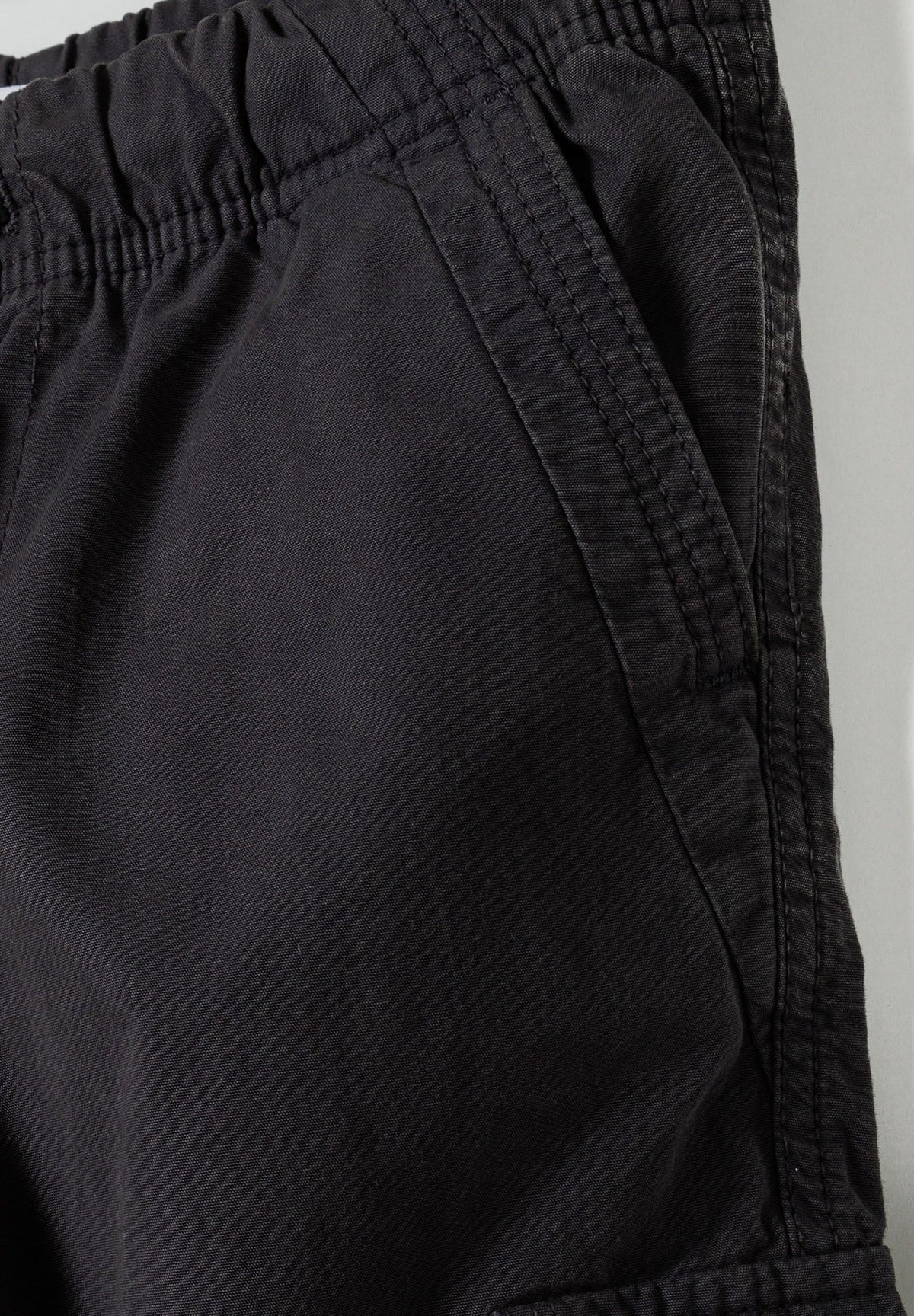 Close-up of black cargo trousers' elasticated waist and angled hip pocket with topstitched edge.