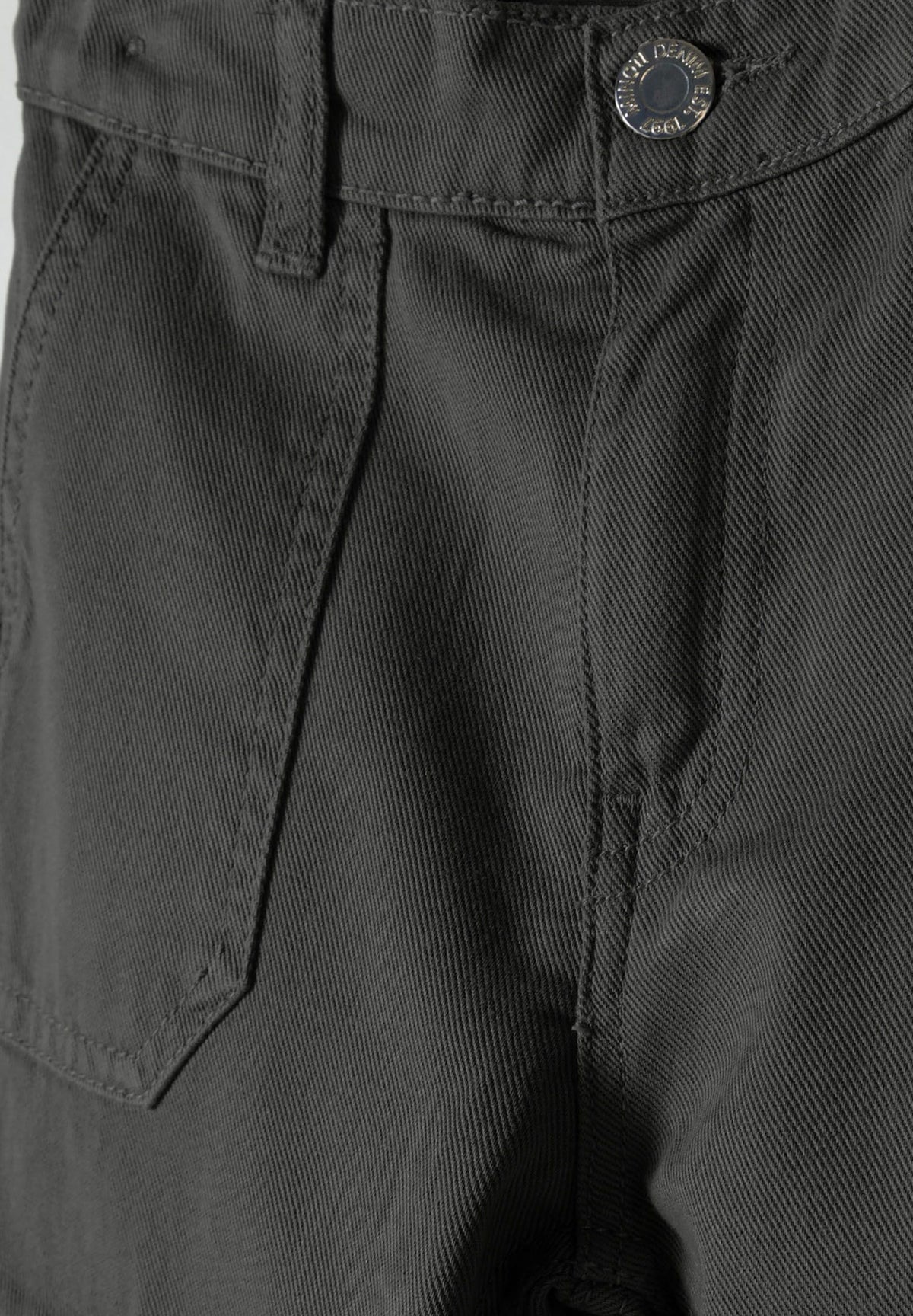 Close-up of dark grey cargo trousers showing the metal waist button, belt loop, front patch pocket and twill texture.