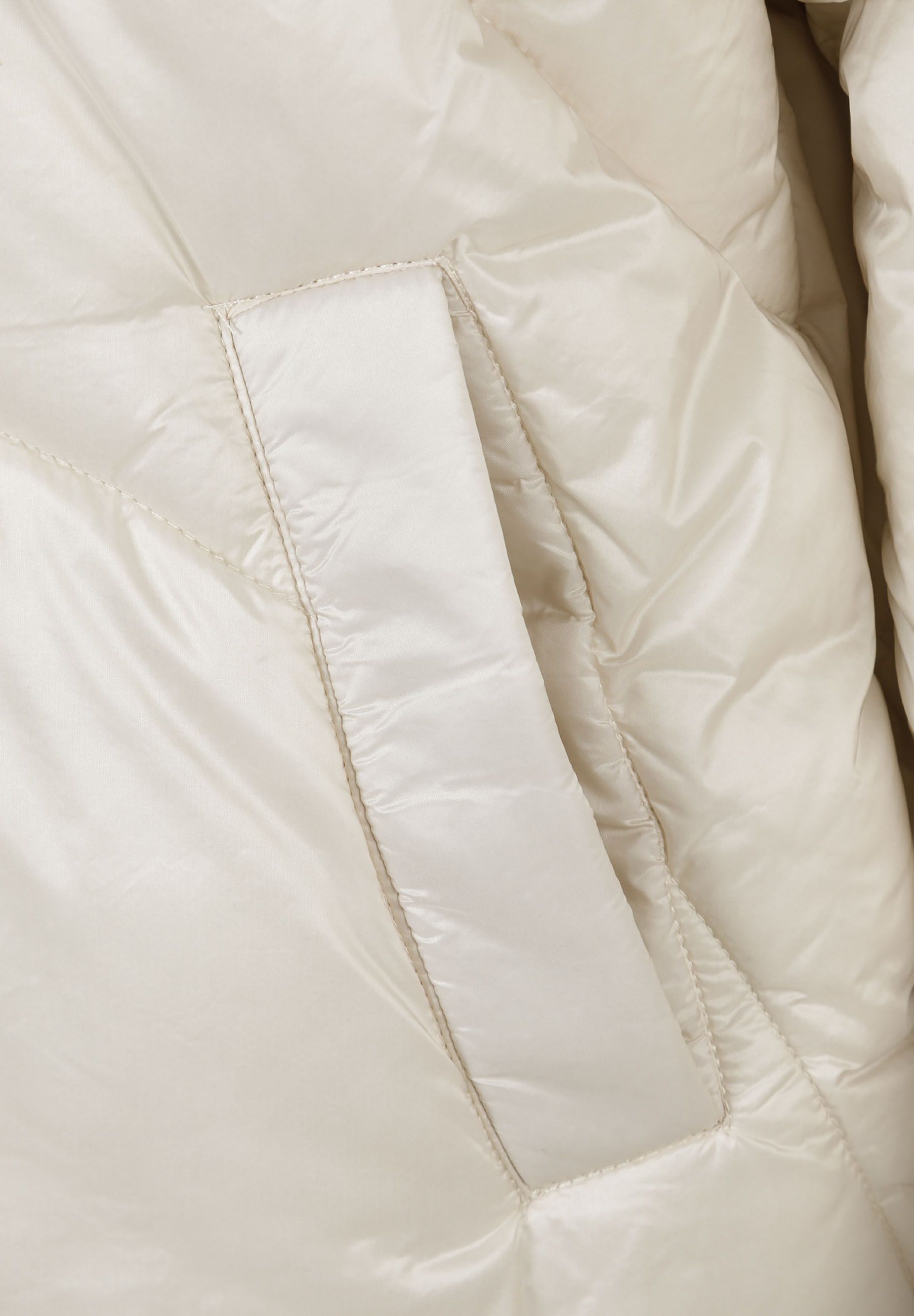 Detail of a short padded women's jacket with curved stitching in a light grey finish.