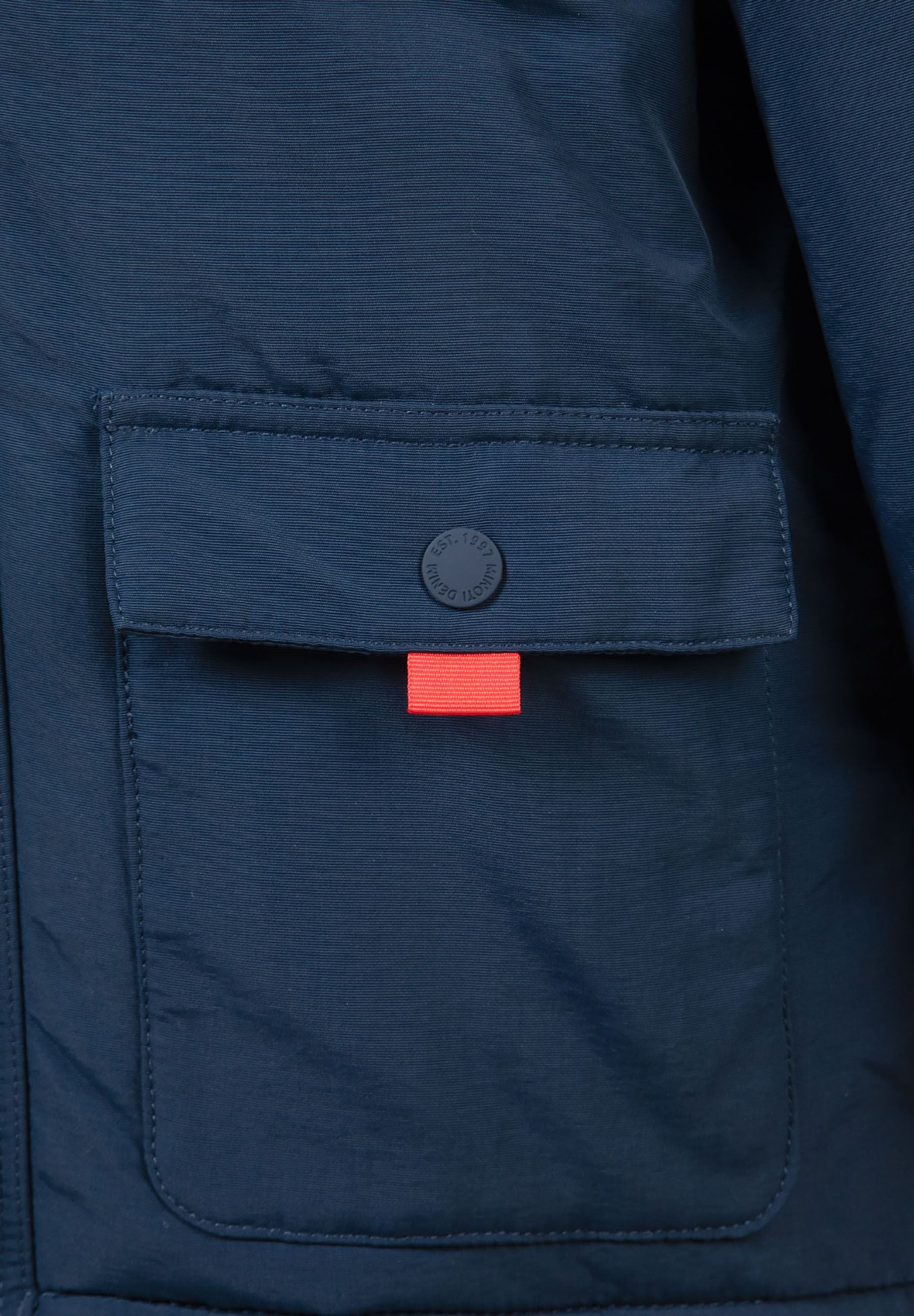 Detail of navy boys winter parka showing flap pocket with snap fastening and red tab.