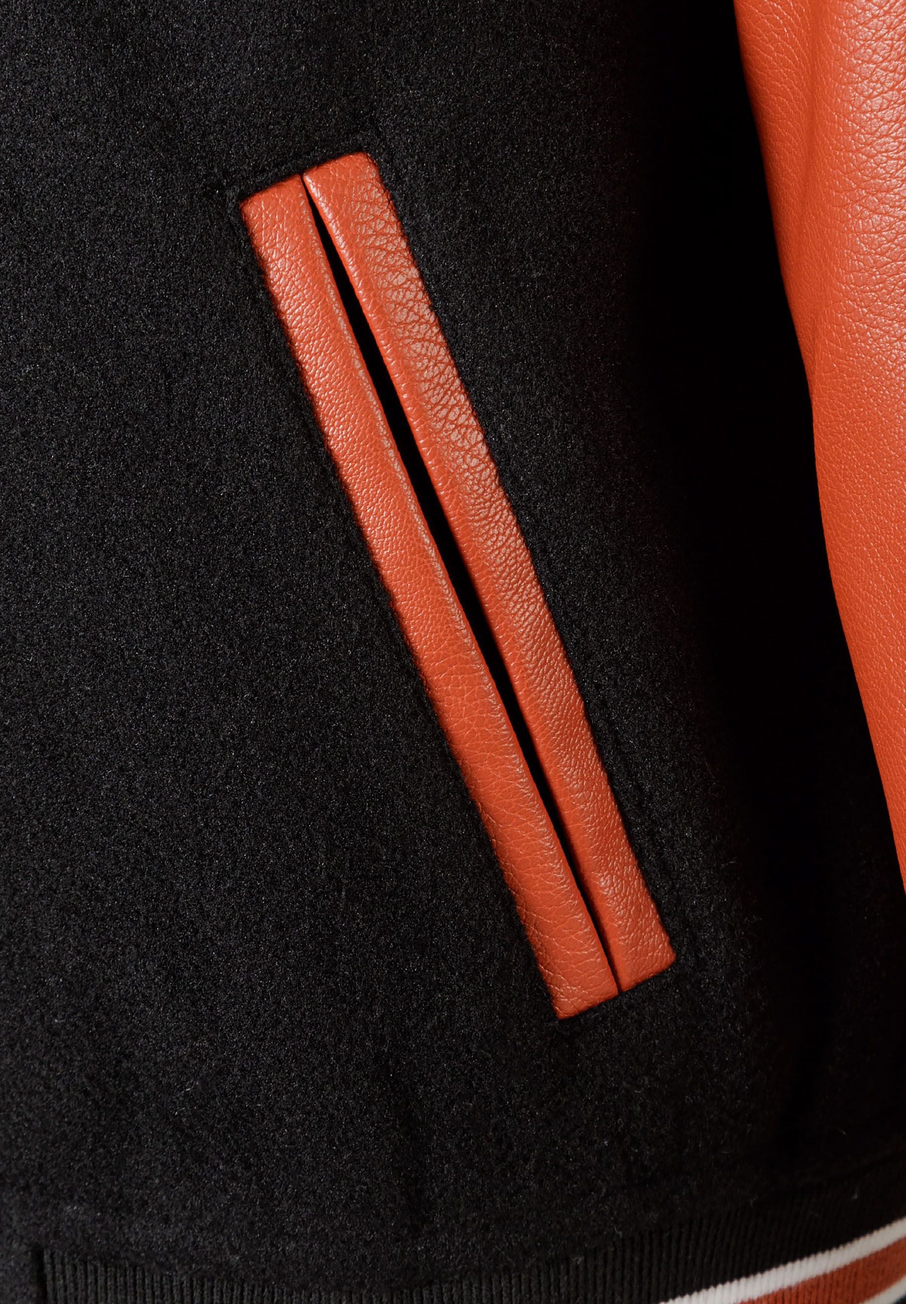 Detail of boys varsity jacket showing black fabric and orange PU sleeve with side pocket.