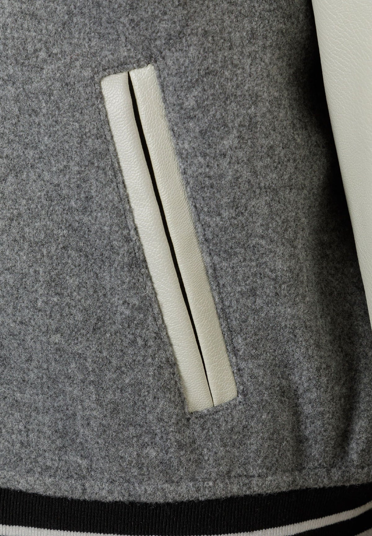 Close-up of a cream leather-look welt pocket on the mottled grey varsity jacket.