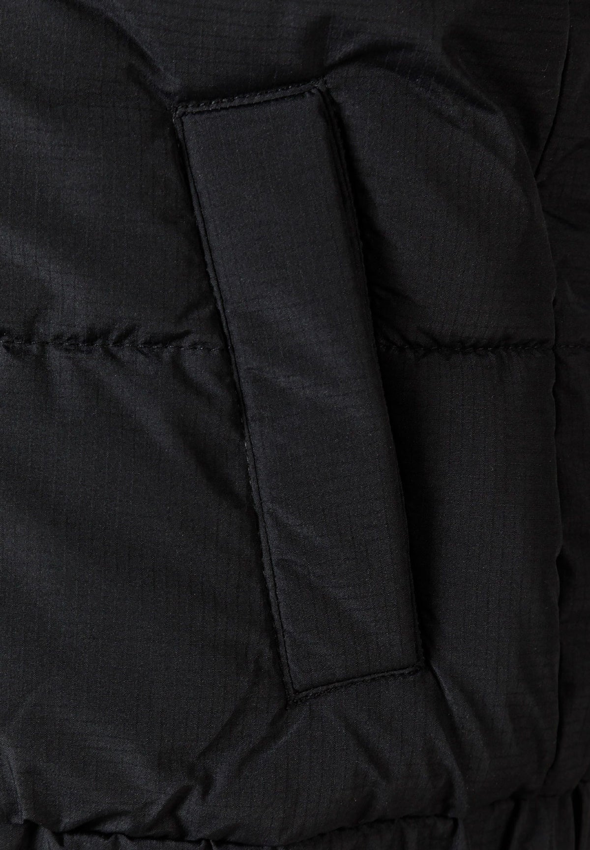 Close-up of a covered vertical side pocket on black quilted gilet.