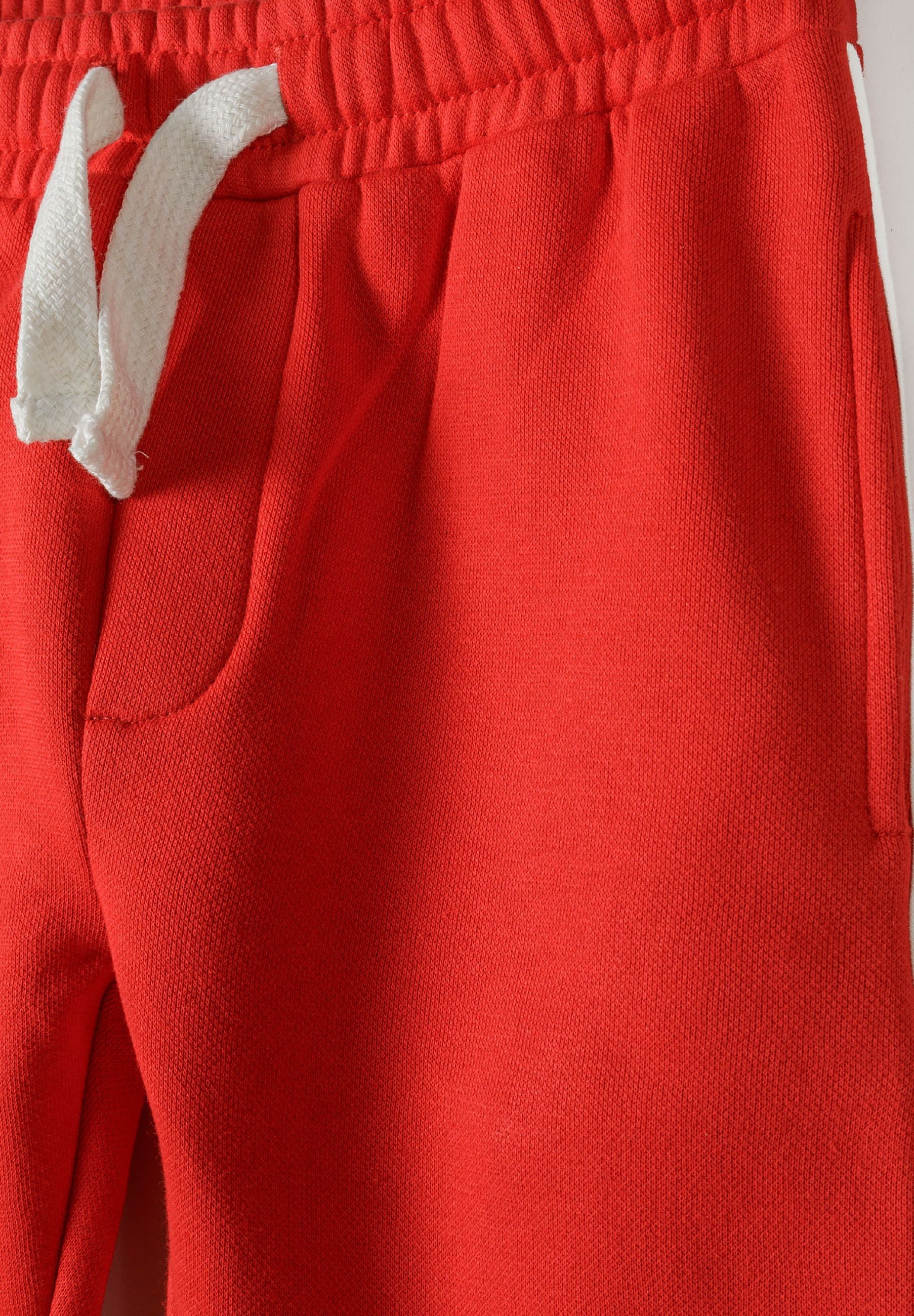 Detail of red joggers with adjustable waistband and side pocket.