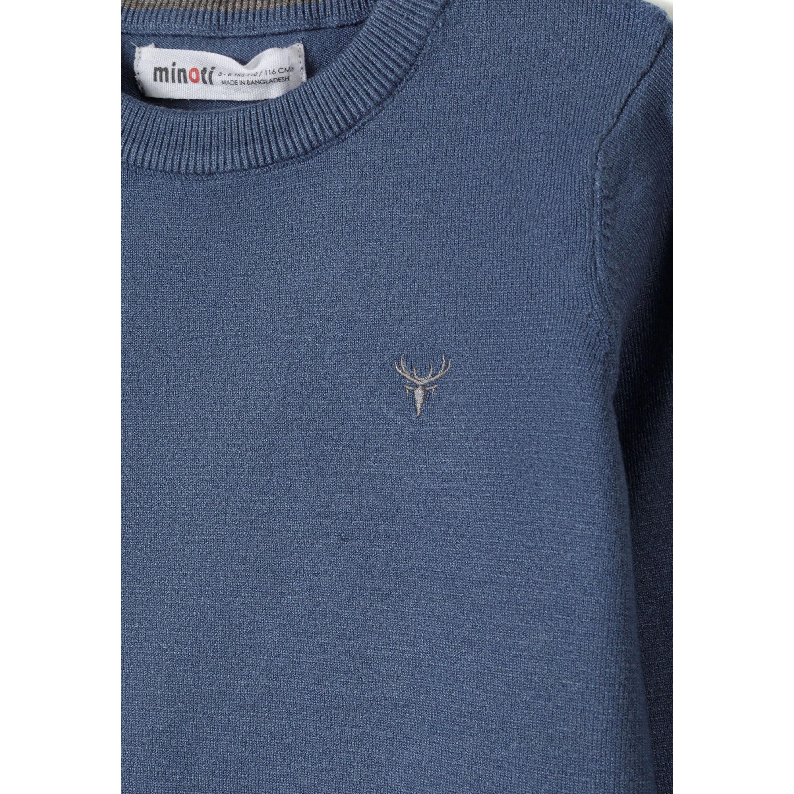 Close-up detail of blue jumper showing Minoti label at neck and small embroidered stag logo on chest