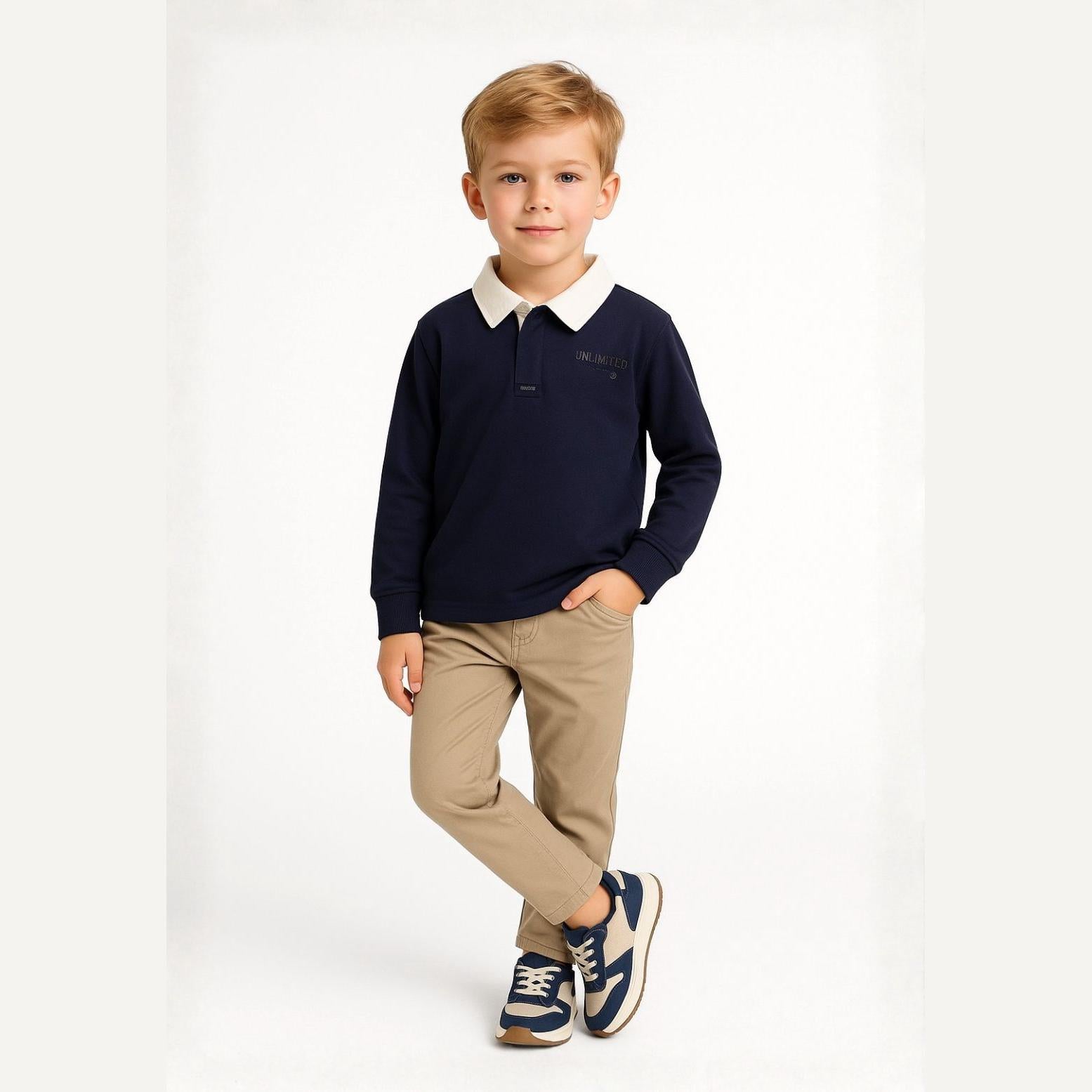 Young blonde boy wearing navy long sleeve polo shirt with white collar and beige chinos, standing against white background