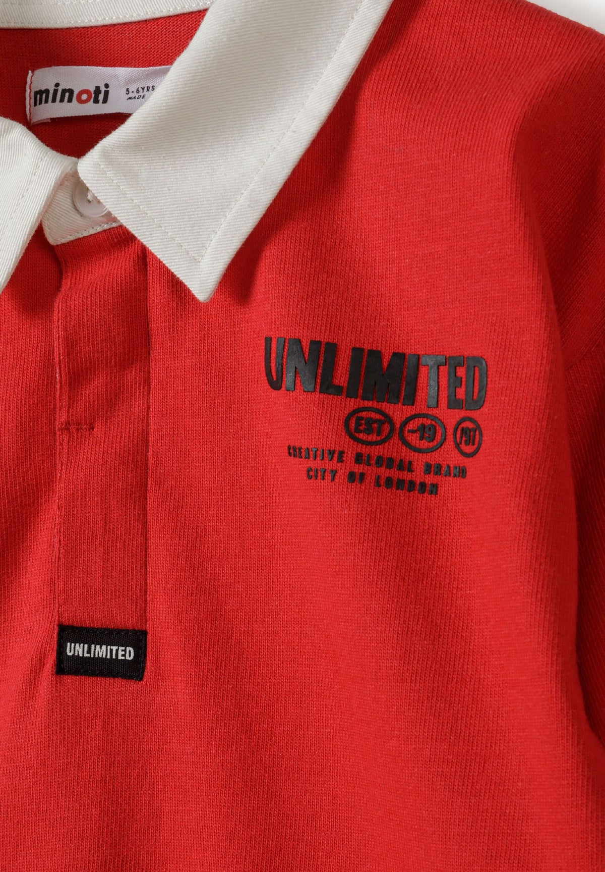 Close-up of red rugby shirt's white collar, covered placket and black UNLIMITED chest print.