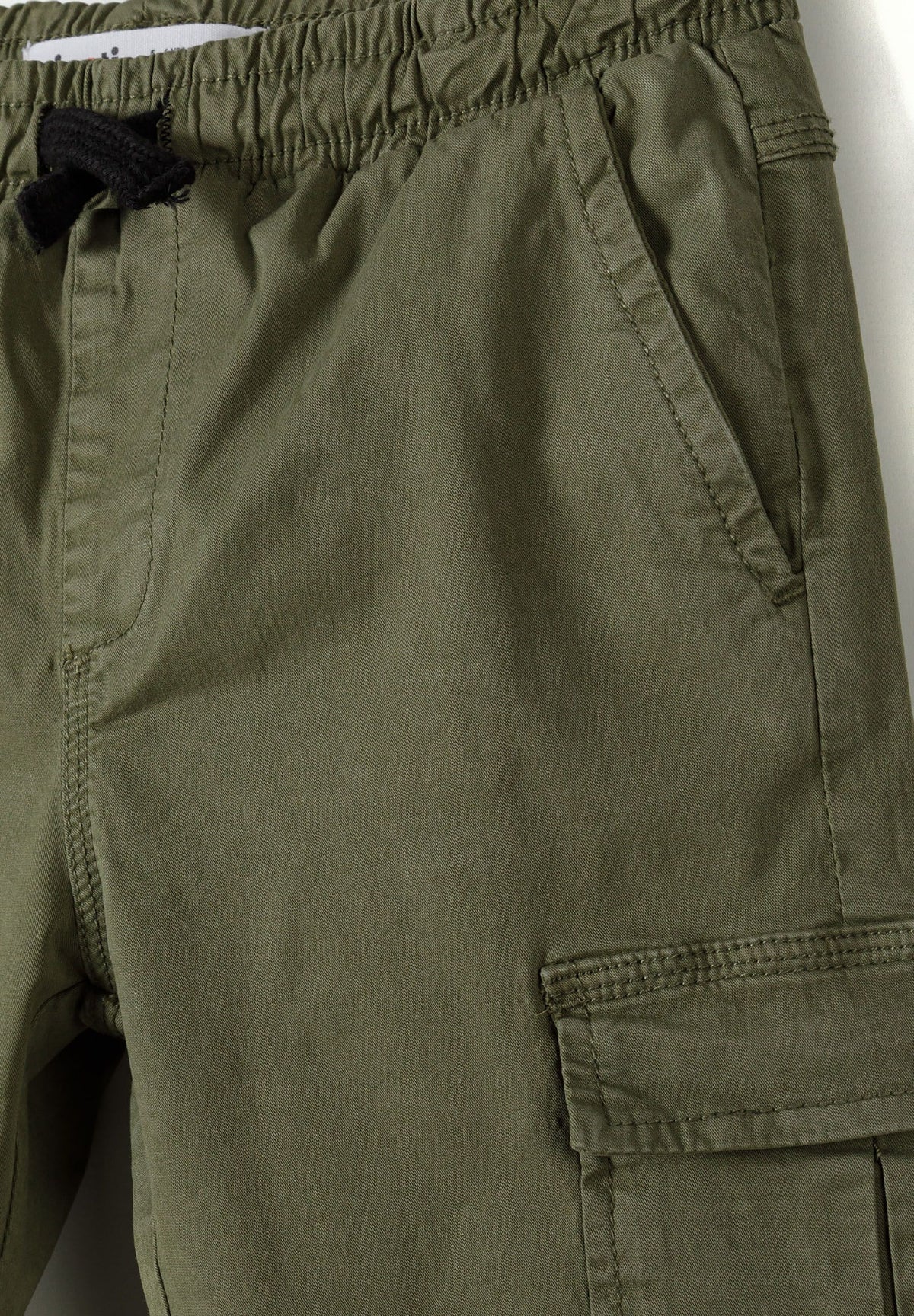 Close-up of khaki cargo trousers' gathered waistband, black drawstring and slanted pocket.