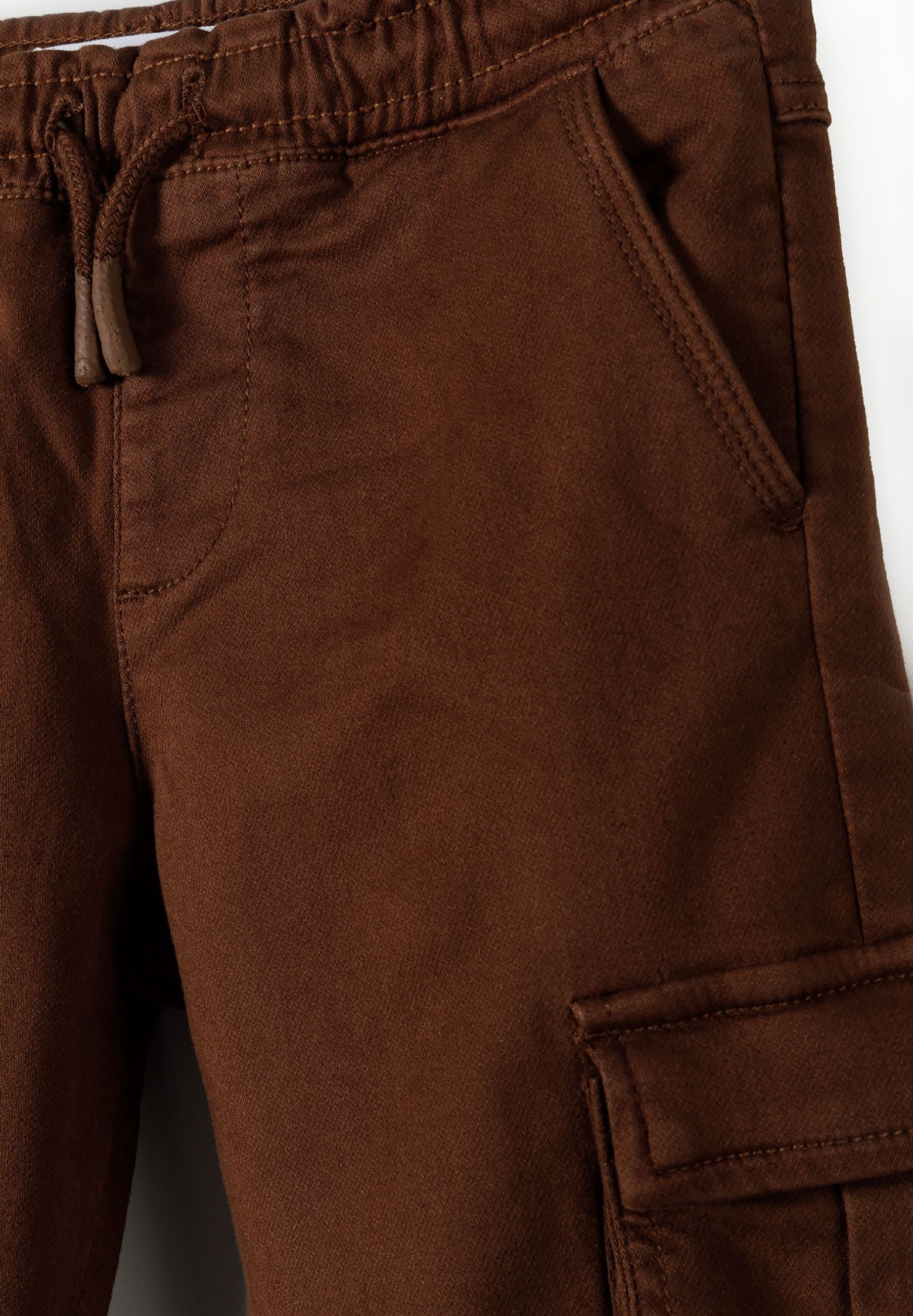 Close-up of brown cargo trousers for boys with elastic waistband and side pockets.
