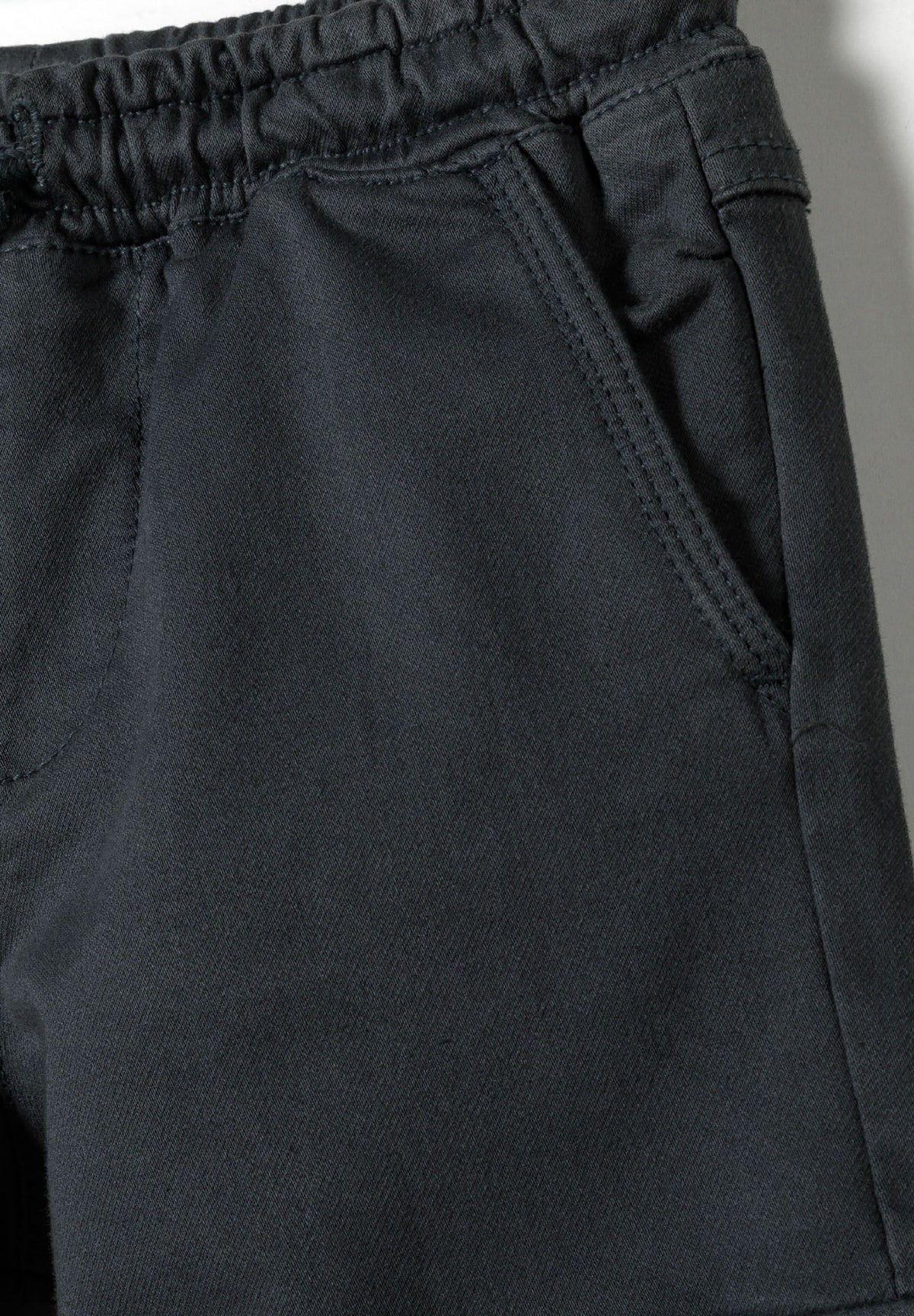 Close-up of open slanted hip pocket and gathered waist on blue-grey cargo trousers.