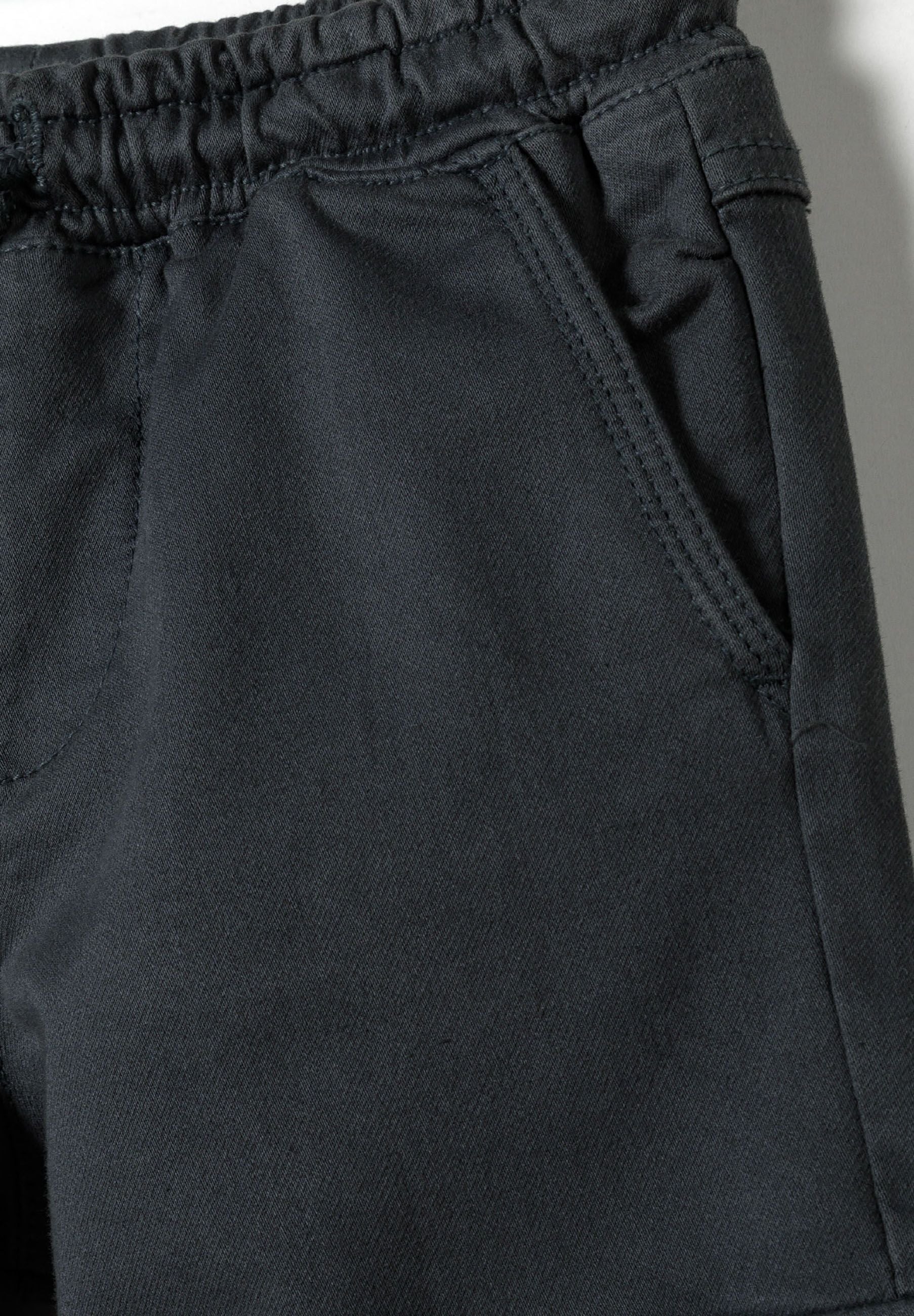 Detail of boys' cargo trousers with elastic waistband and side pocket.