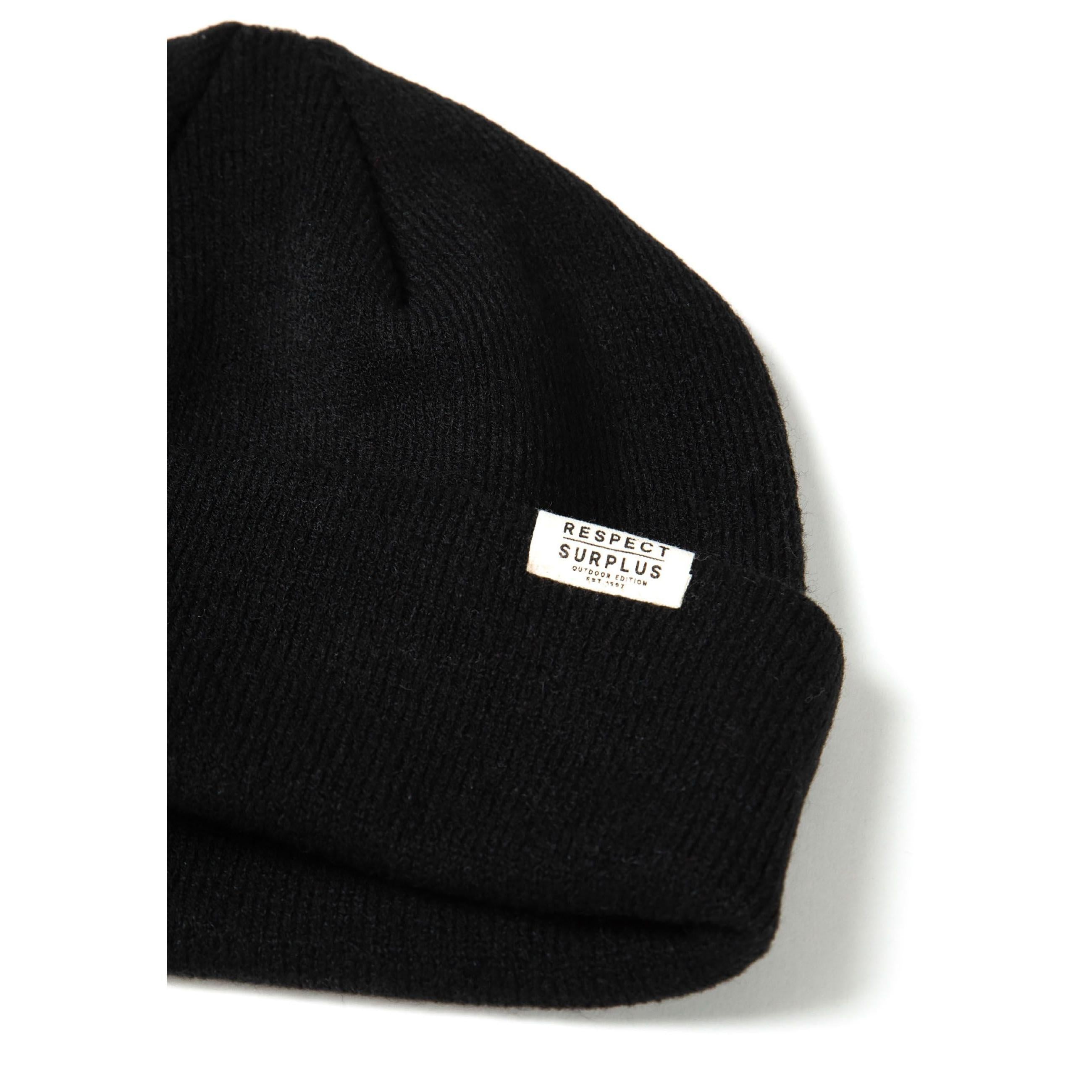 Close-up side view of black ribbed beanie hat showing texture detail and Respect Surplus white label