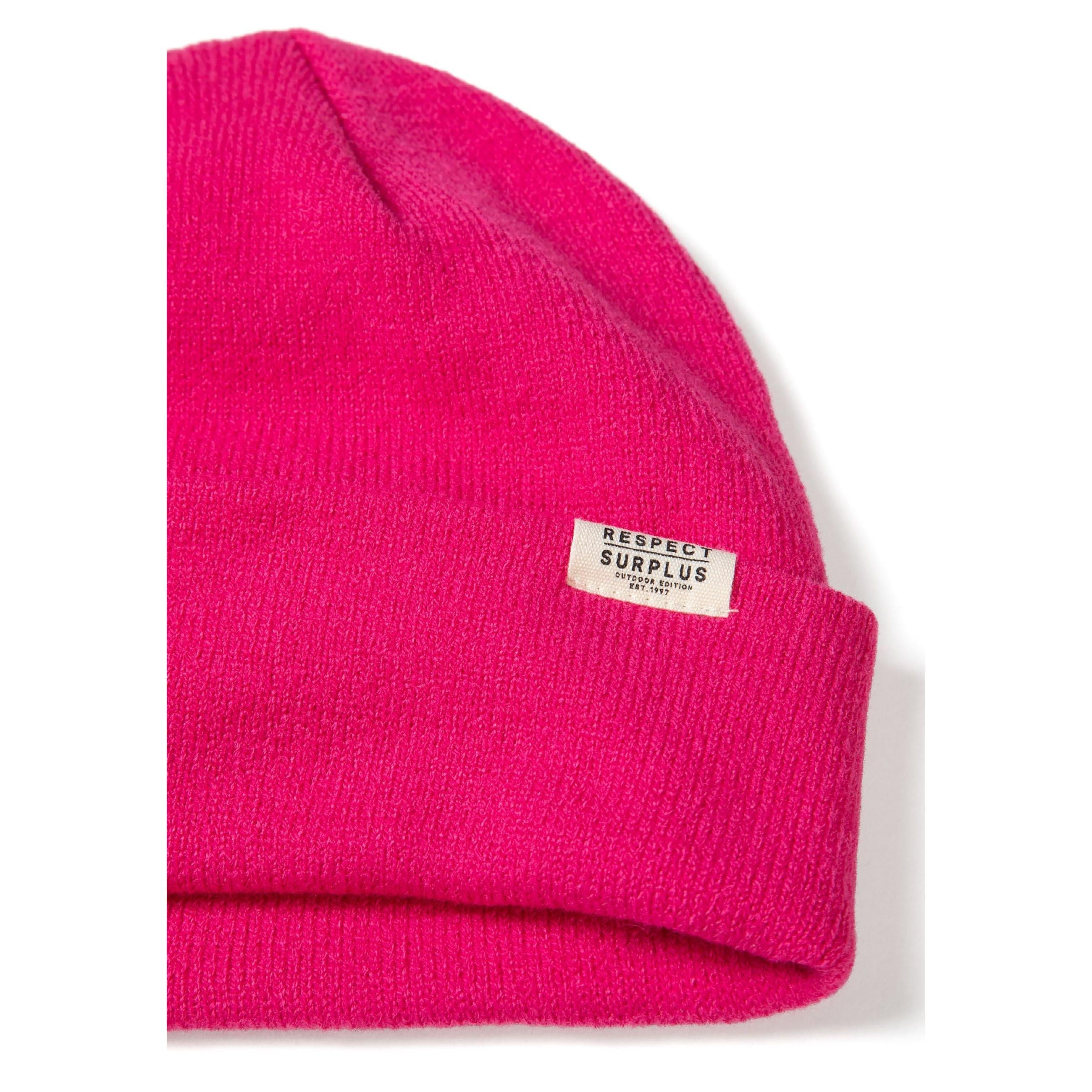 Close-up side view of bright pink ribbed beanie hat showing knit texture and Respect Surplus label