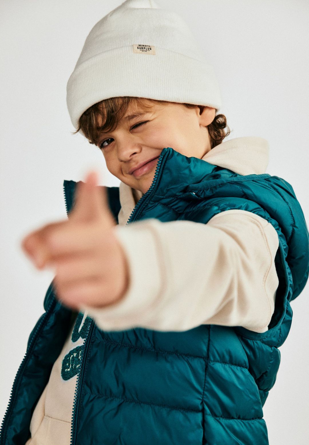 Close-up of a child wearing a white beanie hat with a folded brim and a small badge.