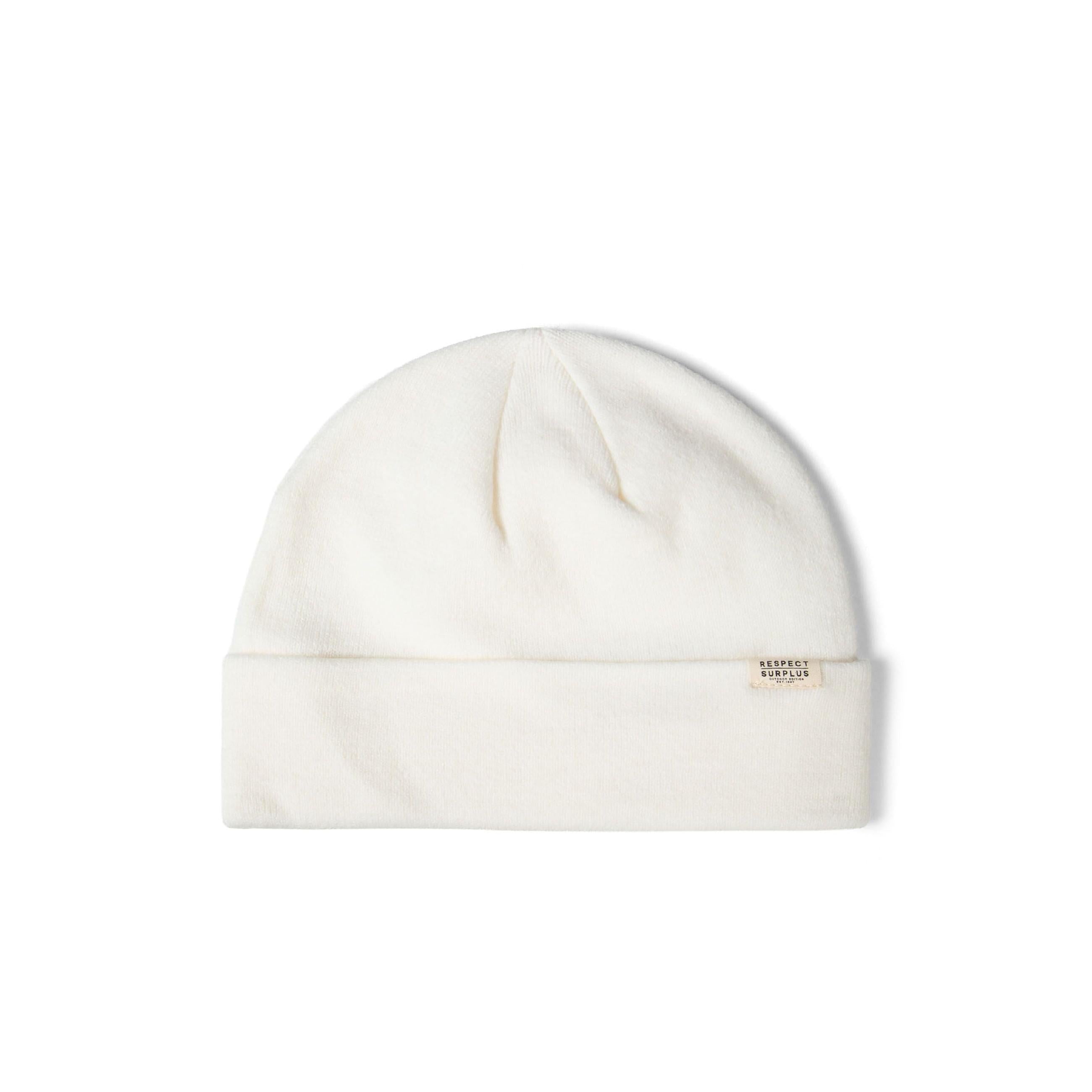 Single cream coloured ribbed knit beanie with folded cuff and small rectangular brand label, photographed flat against white background