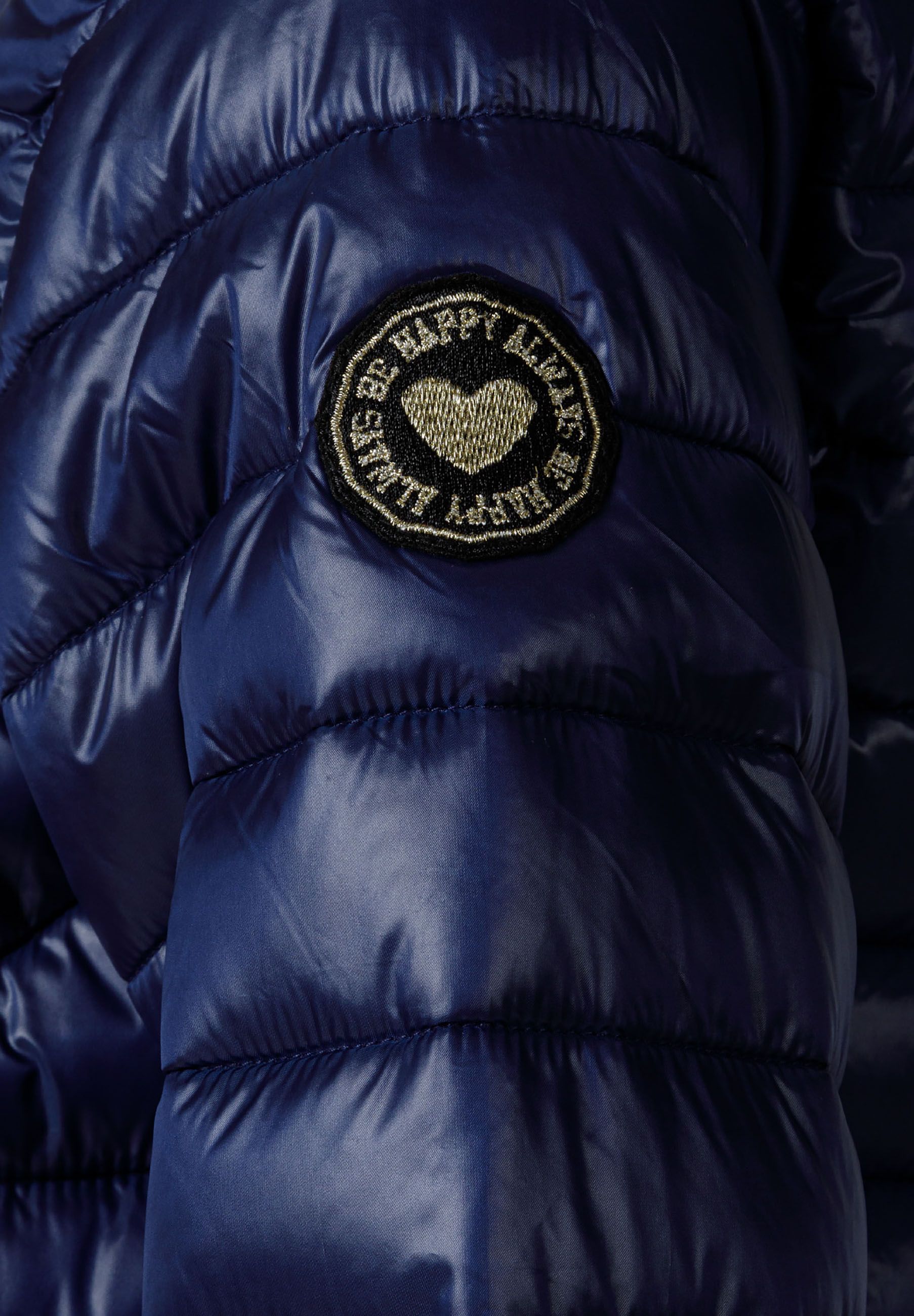 Detail of a navy quilted girls jacket featuring a heart badge.