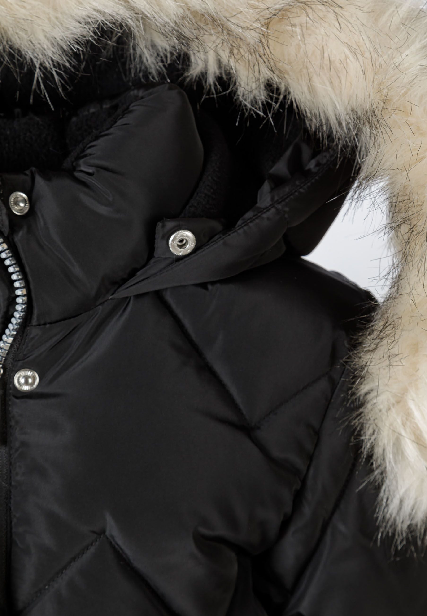 Detail of a black mid-length quilted winter jacket with faux fur hood and snap buttons.