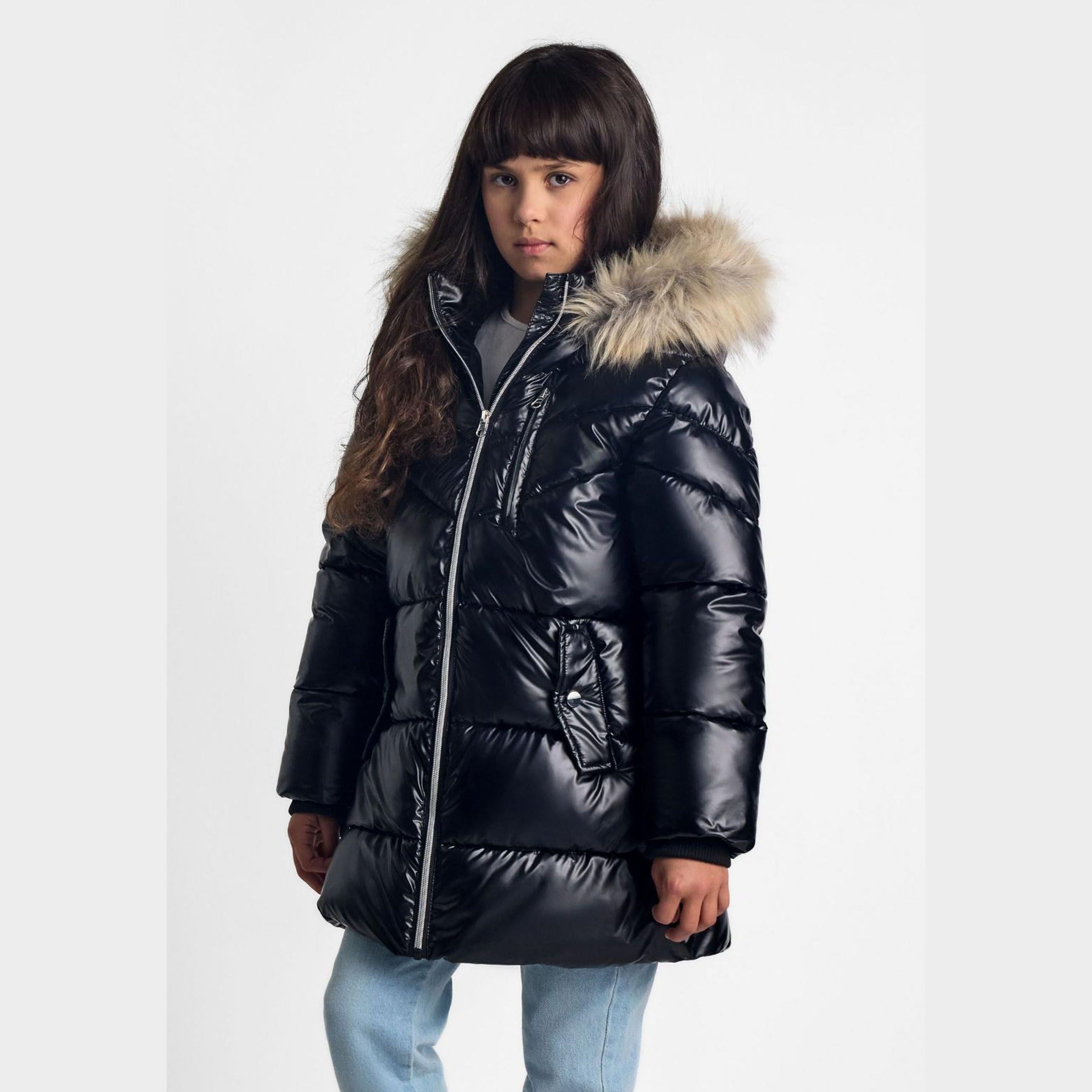 Young model wearing black glossy quilted winter parka with detachable faux fur hood trim, styled with light blue jeans against white studio background