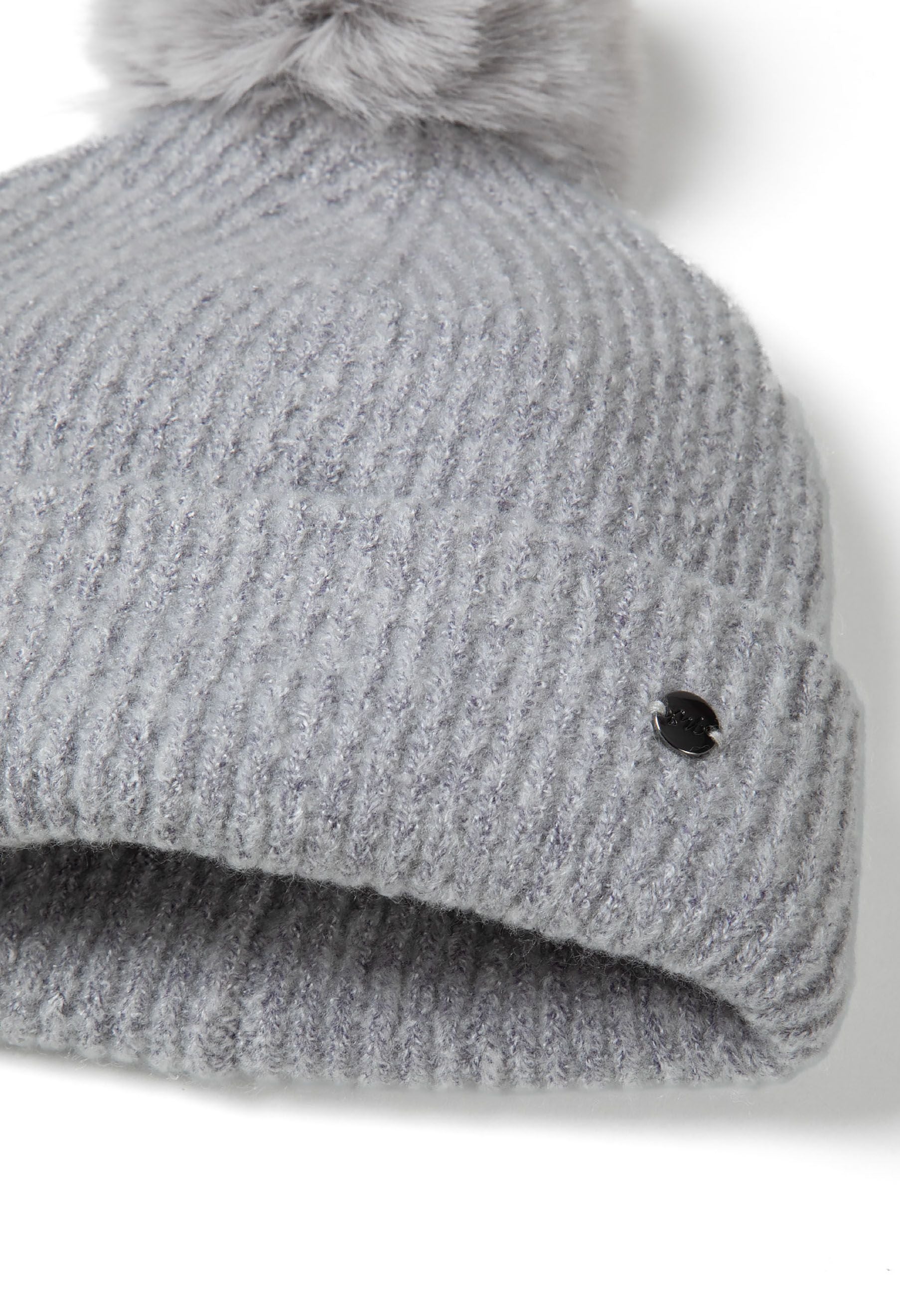 Detail of grey ribbed knit gloves with elasticated cuffs and a metal badge.