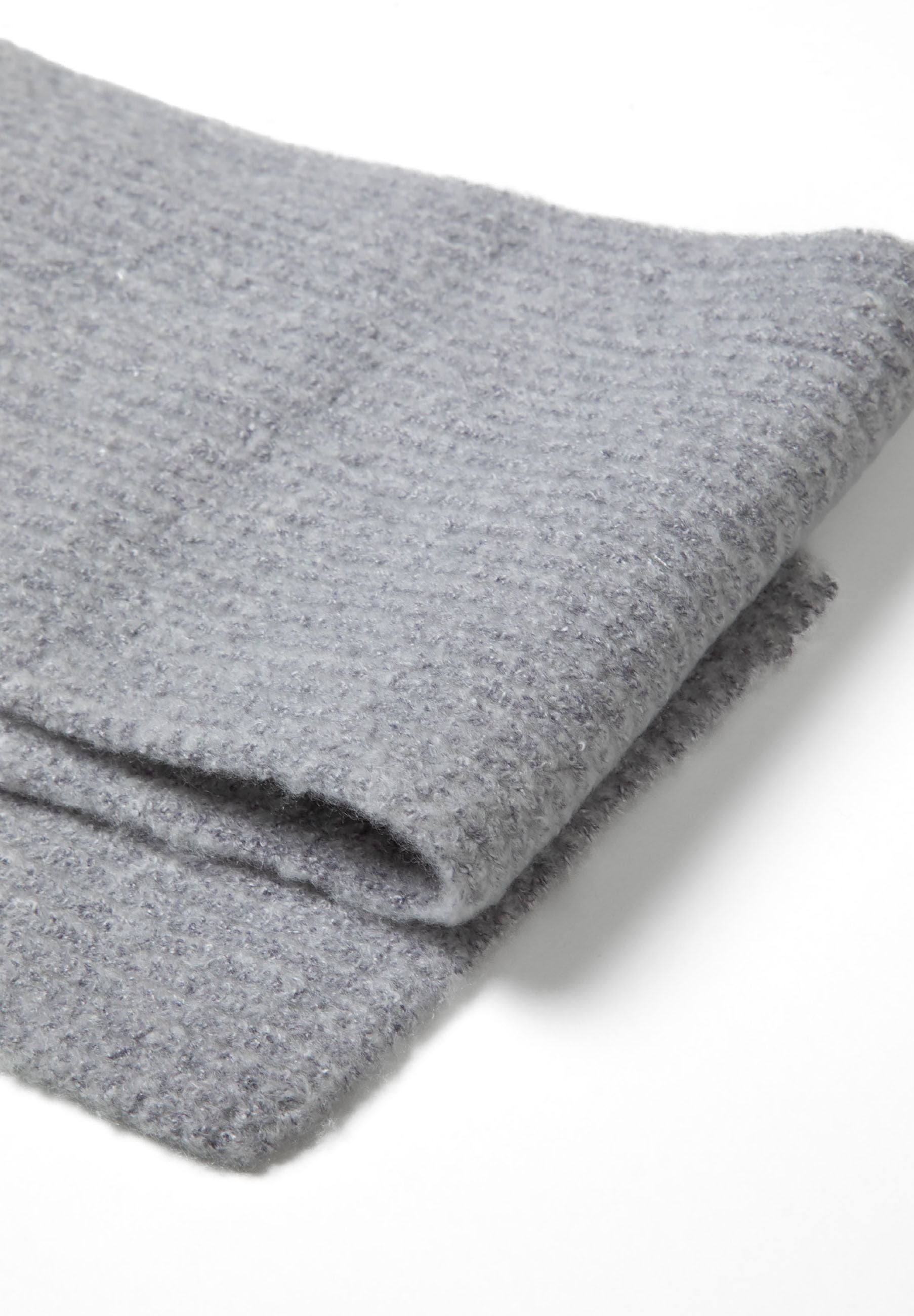Detail of a grey ribbed knit fabric with a black metal badge.
