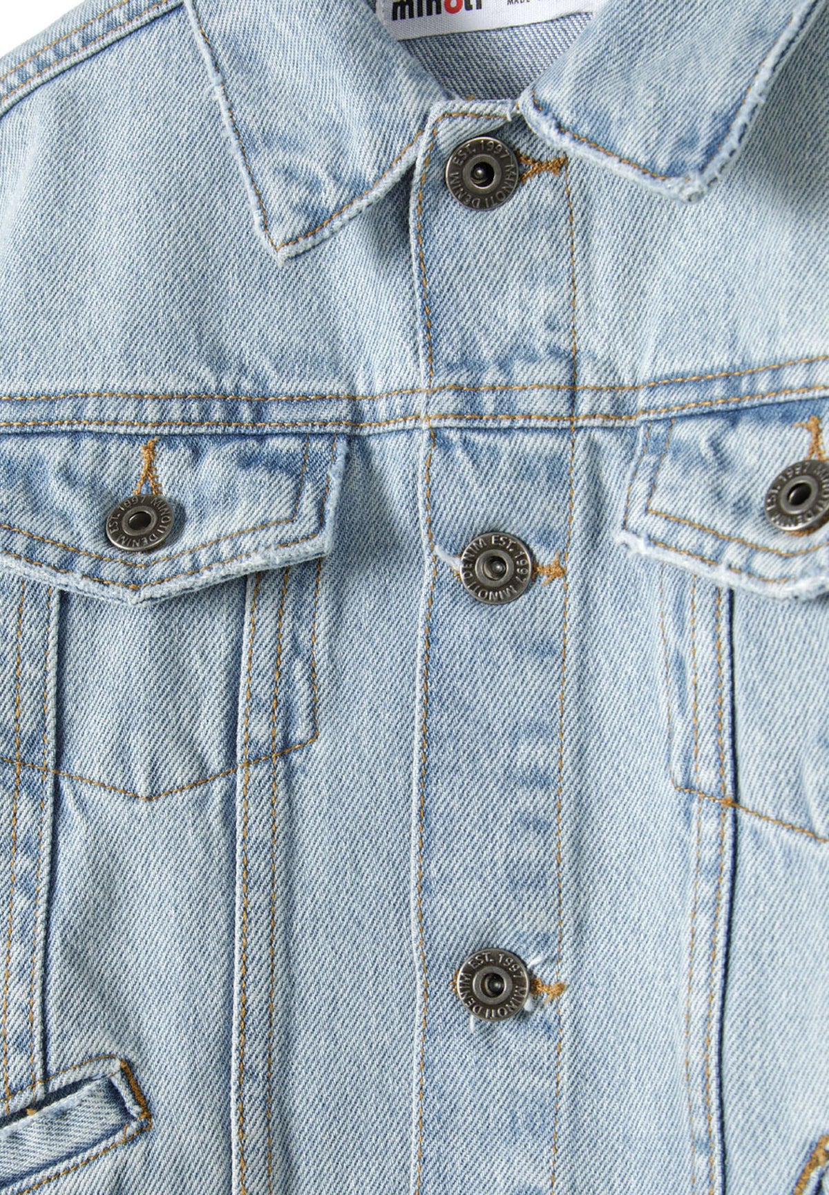 Close-up of light blue denim jacket collar, dark metal buttons and chest flap pockets.