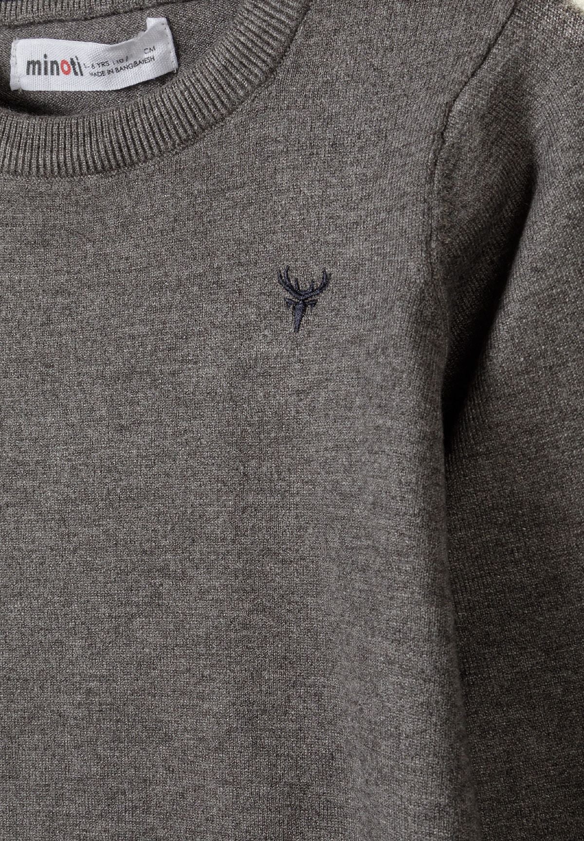 Close-up of grey jumper showing fine-knit texture and small dark antler embroidery.