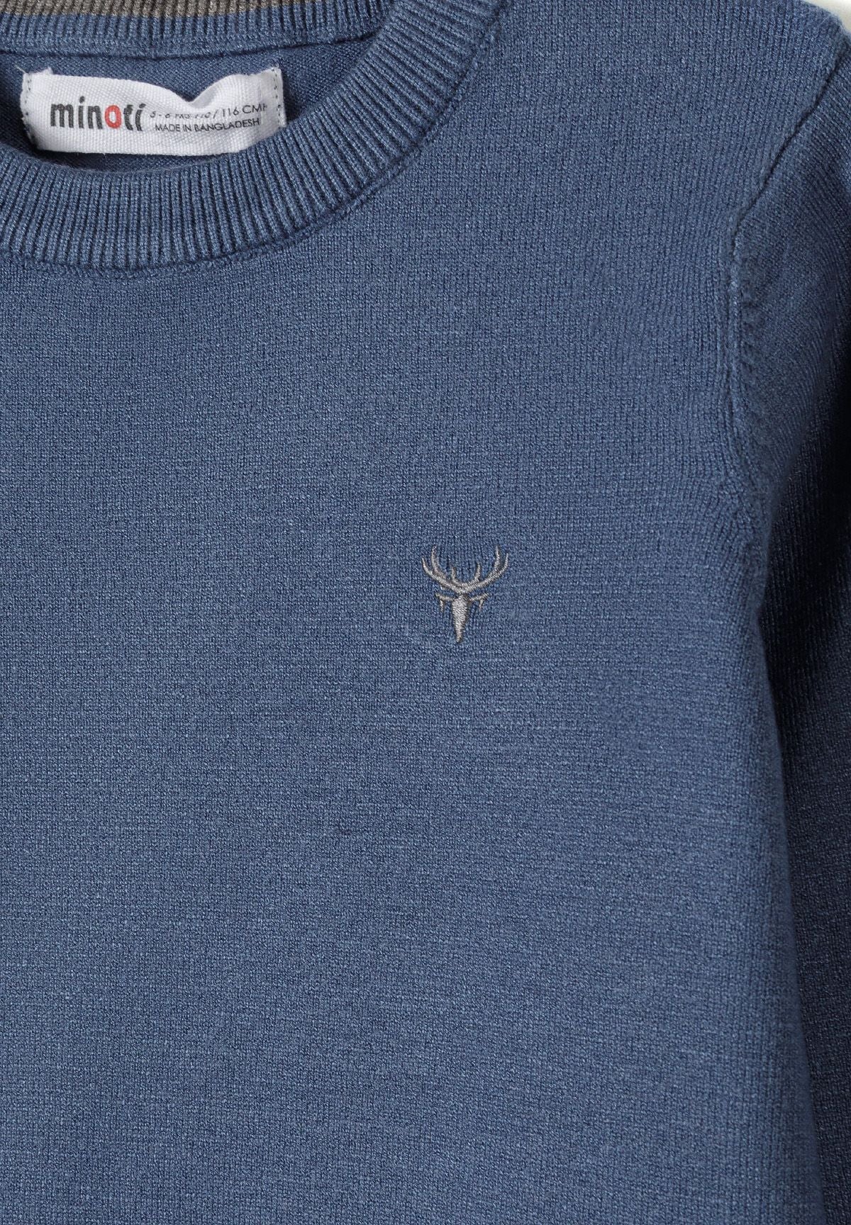 Close-up of blue jumper's ribbed neckline and pale embroidered stag-head motif.