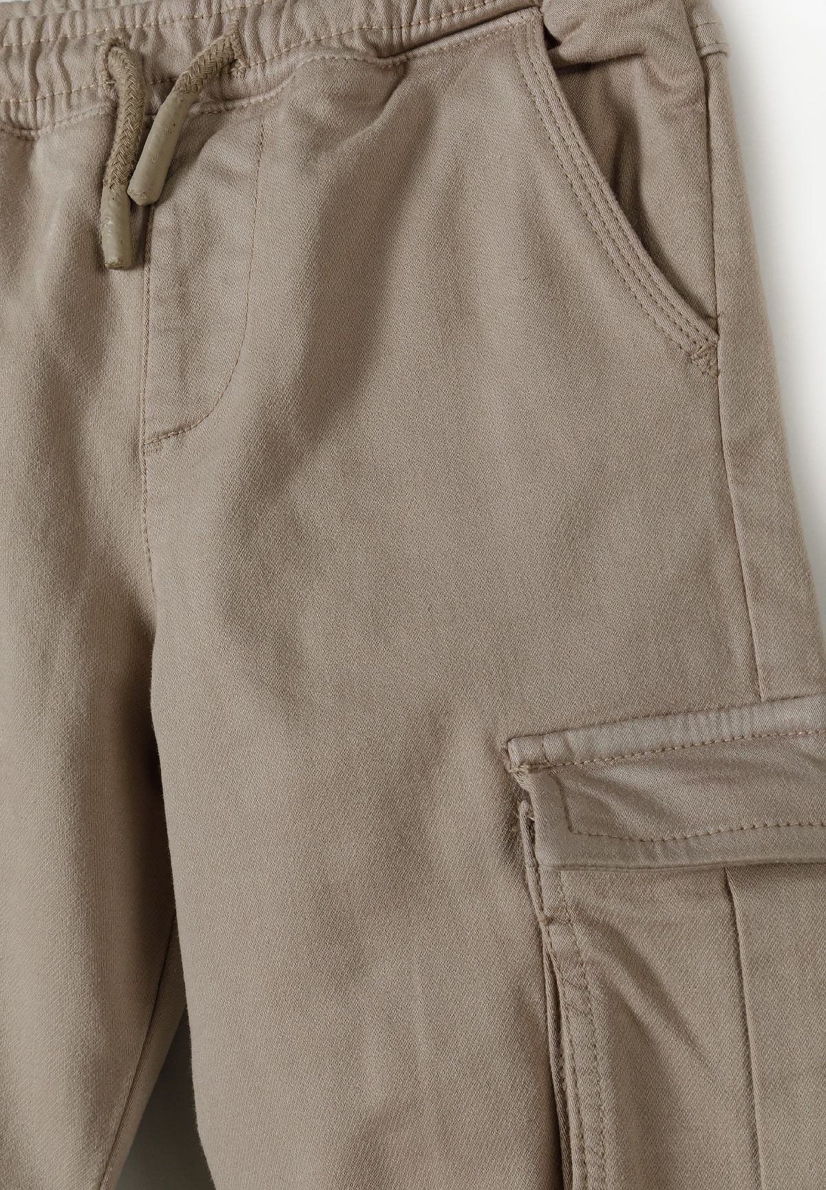 Close-up of beige cargo trouser waistband, drawstring, hip pocket and thigh flap.