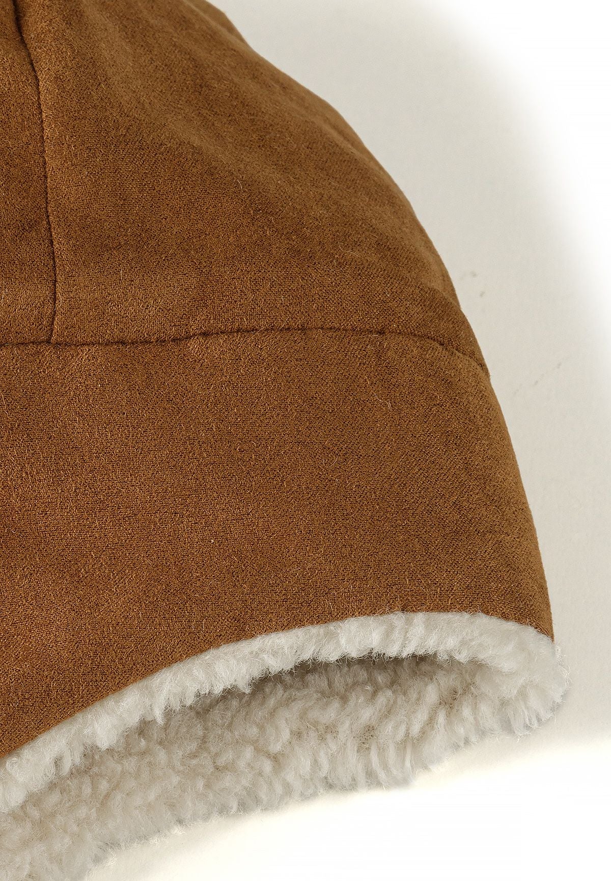 Close-up of the tan trapper hat's smooth outer panel and cream fluffy edge lining.