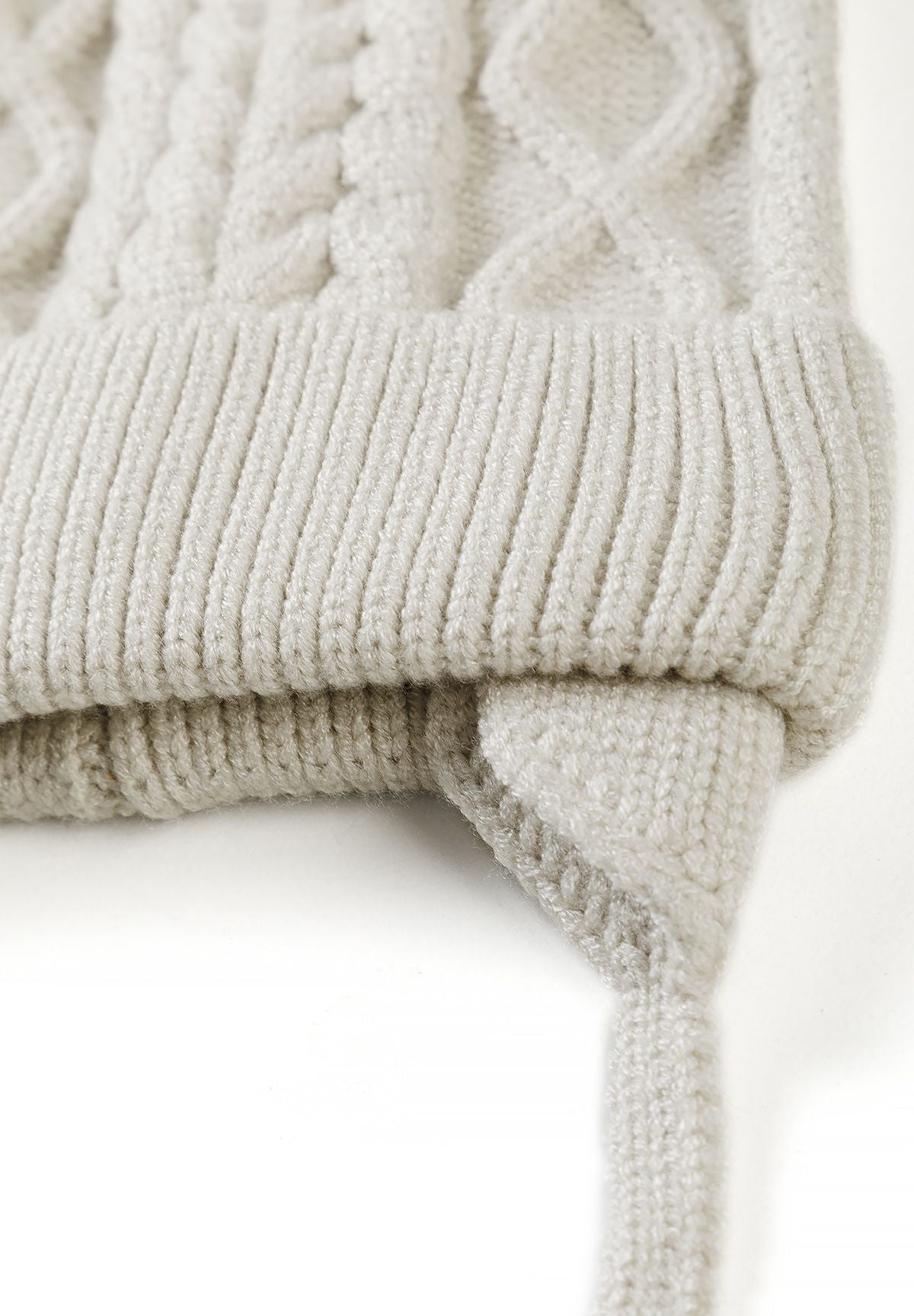 Close-up of the cream hat's folded rib-knit brim, shaped earflap and knitted tie.